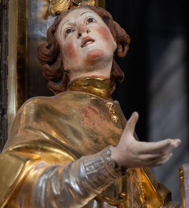 Zdjęcie nr 47: Ołtarz drewniany, prostopadłościenny z kamienną mensą, z kamiennym portatylem. Antepedium drewniane ujęte marmoryzowaną ramą z karbowanym profilem. W polu owalny medalion z przedstawieniem świętego z zakonu Marków, ujętym wicią akantową przeplatana z kwiatową. Nastawa ołtarzowa architektoniczna, jednoosiowa, jednokondygnacyjna ze zwieńczeniem na cokole.  Retabulum flankowane parą zdwojonych półfilarów zakończonych konsolami,  dźwigających pełne belkowanie oraz fragmenty przerwanego, półkolistego przyczółka z siedzącymi puttami. Na tle pilastrów, na konsolach ustawione figury dwóch świętych. Trzony pilastrów dekorowane kampanulami. W polu środkowym wnęka w formie stojącego prostokąta zamkniętego łukiem segmentowym nadwieszonego z uskokiem ujęta profilowaną ramą, z obrazem Wskrzeszenie Łazarza, w osobnej ramie. Nad wnęką baldachim dekorowany lambrekinem, z podwieszoną tkaniną po dwóch stronach, lamowaną frędzlą. Nam baldachimem kartusz z uskrzydlonymi główkami anielskimi i zwieńczony koroną. Zwieńczenie w formie zbliżonej do trapezu o wklęsłych bokach zamknięte falistym gzymsem, dekorowanym kampanulami. W polu gorejące serce przebite mieczem, w otoku z obłoków i uskrzydlonych główek anielskich, w glorii promienistej.  Struktura polichromowana w sposób imitujący marmoryzację w kolorze beżowo-zielonym. Ornamentyka i profile złocone, detal i zwieńczenie srebrzone.