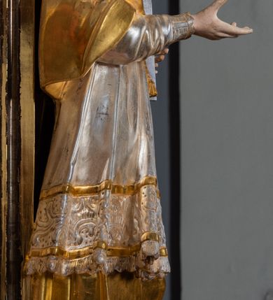 Zdjęcie nr 49: Ołtarz drewniany, prostopadłościenny z kamienną mensą, z kamiennym portatylem. Antepedium drewniane ujęte marmoryzowaną ramą z karbowanym profilem. W polu owalny medalion z przedstawieniem świętego z zakonu Marków, ujętym wicią akantową przeplatana z kwiatową. Nastawa ołtarzowa architektoniczna, jednoosiowa, jednokondygnacyjna ze zwieńczeniem na cokole.  Retabulum flankowane parą zdwojonych półfilarów zakończonych konsolami,  dźwigających pełne belkowanie oraz fragmenty przerwanego, półkolistego przyczółka z siedzącymi puttami. Na tle pilastrów, na konsolach ustawione figury dwóch świętych. Trzony pilastrów dekorowane kampanulami. W polu środkowym wnęka w formie stojącego prostokąta zamkniętego łukiem segmentowym nadwieszonego z uskokiem ujęta profilowaną ramą, z obrazem Wskrzeszenie Łazarza, w osobnej ramie. Nad wnęką baldachim dekorowany lambrekinem, z podwieszoną tkaniną po dwóch stronach, lamowaną frędzlą. Nam baldachimem kartusz z uskrzydlonymi główkami anielskimi i zwieńczony koroną. Zwieńczenie w formie zbliżonej do trapezu o wklęsłych bokach zamknięte falistym gzymsem, dekorowanym kampanulami. W polu gorejące serce przebite mieczem, w otoku z obłoków i uskrzydlonych główek anielskich, w glorii promienistej.  Struktura polichromowana w sposób imitujący marmoryzację w kolorze beżowo-zielonym. Ornamentyka i profile złocone, detal i zwieńczenie srebrzone.