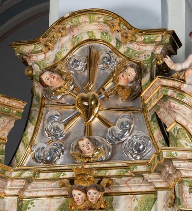 Zdjęcie nr 51: Ołtarz drewniany, prostopadłościenny z kamienną mensą, z kamiennym portatylem. Antepedium drewniane ujęte marmoryzowaną ramą z karbowanym profilem. W polu owalny medalion z przedstawieniem świętego z zakonu Marków, ujętym wicią akantową przeplatana z kwiatową. Nastawa ołtarzowa architektoniczna, jednoosiowa, jednokondygnacyjna ze zwieńczeniem na cokole.  Retabulum flankowane parą zdwojonych półfilarów zakończonych konsolami,  dźwigających pełne belkowanie oraz fragmenty przerwanego, półkolistego przyczółka z siedzącymi puttami. Na tle pilastrów, na konsolach ustawione figury dwóch świętych. Trzony pilastrów dekorowane kampanulami. W polu środkowym wnęka w formie stojącego prostokąta zamkniętego łukiem segmentowym nadwieszonego z uskokiem ujęta profilowaną ramą, z obrazem Wskrzeszenie Łazarza, w osobnej ramie. Nad wnęką baldachim dekorowany lambrekinem, z podwieszoną tkaniną po dwóch stronach, lamowaną frędzlą. Nam baldachimem kartusz z uskrzydlonymi główkami anielskimi i zwieńczony koroną. Zwieńczenie w formie zbliżonej do trapezu o wklęsłych bokach zamknięte falistym gzymsem, dekorowanym kampanulami. W polu gorejące serce przebite mieczem, w otoku z obłoków i uskrzydlonych główek anielskich, w glorii promienistej.  Struktura polichromowana w sposób imitujący marmoryzację w kolorze beżowo-zielonym. Ornamentyka i profile złocone, detal i zwieńczenie srebrzone.