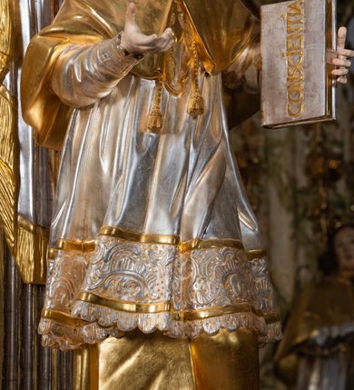 Zdjęcie nr 60: Ołtarz drewniany, prostopadłościenny z kamienną mensą, z kamiennym portatylem. Antepedium drewniane ujęte marmoryzowaną ramą z karbowanym profilem. W polu owalny medalion z przedstawieniem świętego z zakonu Marków, ujętym wicią akantową przeplatana z kwiatową. Nastawa ołtarzowa architektoniczna, jednoosiowa, jednokondygnacyjna ze zwieńczeniem na cokole.  Retabulum flankowane parą zdwojonych półfilarów zakończonych konsolami,  dźwigających pełne belkowanie oraz fragmenty przerwanego, półkolistego przyczółka z siedzącymi puttami. Na tle pilastrów, na konsolach ustawione figury dwóch świętych. Trzony pilastrów dekorowane kampanulami. W polu środkowym wnęka w formie stojącego prostokąta zamkniętego łukiem segmentowym nadwieszonego z uskokiem ujęta profilowaną ramą, z obrazem Wskrzeszenie Łazarza, w osobnej ramie. Nad wnęką baldachim dekorowany lambrekinem, z podwieszoną tkaniną po dwóch stronach, lamowaną frędzlą. Nam baldachimem kartusz z uskrzydlonymi główkami anielskimi i zwieńczony koroną. Zwieńczenie w formie zbliżonej do trapezu o wklęsłych bokach zamknięte falistym gzymsem, dekorowanym kampanulami. W polu gorejące serce przebite mieczem, w otoku z obłoków i uskrzydlonych główek anielskich, w glorii promienistej.  Struktura polichromowana w sposób imitujący marmoryzację w kolorze beżowo-zielonym. Ornamentyka i profile złocone, detal i zwieńczenie srebrzone.