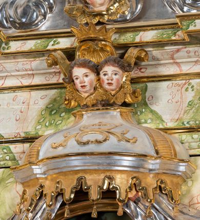 Zdjęcie nr 62: Ołtarz drewniany, prostopadłościenny z kamienną mensą, z kamiennym portatylem. Antepedium drewniane ujęte marmoryzowaną ramą z karbowanym profilem. W polu owalny medalion z przedstawieniem świętego z zakonu Marków, ujętym wicią akantową przeplatana z kwiatową. Nastawa ołtarzowa architektoniczna, jednoosiowa, jednokondygnacyjna ze zwieńczeniem na cokole.  Retabulum flankowane parą zdwojonych półfilarów zakończonych konsolami,  dźwigających pełne belkowanie oraz fragmenty przerwanego, półkolistego przyczółka z siedzącymi puttami. Na tle pilastrów, na konsolach ustawione figury dwóch świętych. Trzony pilastrów dekorowane kampanulami. W polu środkowym wnęka w formie stojącego prostokąta zamkniętego łukiem segmentowym nadwieszonego z uskokiem ujęta profilowaną ramą, z obrazem Wskrzeszenie Łazarza, w osobnej ramie. Nad wnęką baldachim dekorowany lambrekinem, z podwieszoną tkaniną po dwóch stronach, lamowaną frędzlą. Nam baldachimem kartusz z uskrzydlonymi główkami anielskimi i zwieńczony koroną. Zwieńczenie w formie zbliżonej do trapezu o wklęsłych bokach zamknięte falistym gzymsem, dekorowanym kampanulami. W polu gorejące serce przebite mieczem, w otoku z obłoków i uskrzydlonych główek anielskich, w glorii promienistej.  Struktura polichromowana w sposób imitujący marmoryzację w kolorze beżowo-zielonym. Ornamentyka i profile złocone, detal i zwieńczenie srebrzone.
