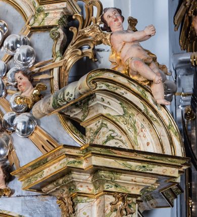 Zdjęcie nr 15: Ołtarz drewniany, prostopadłościenny z kamienną mensą, z kamiennym portatylem. Antepedium z prostokątną płyciną ujętą marmoryzowaną ramą ze złoconym karbowanym profilem. W polu przedstawienie świętej z aniołkiem podającym jej kosz kwiatów, flankowany akantową wicią akantową przeplataną z roślinną, na jasnoniebieskim tle, z datą „1754”. Nastawa ołtarzowa architektoniczna, jednoosiowa, jednokondygnacyjna ze zwieńczeniem na dwustrefowym cokole.  Retabulum flankowane parą opilastrowanych filarów, które dźwigają imposty oraz fragmenty przerwanego półkolistego przyczółka z siedzącymi puttami. Na tle filarów, na konsolach ustawione 2 figury św. Demetriusza i św. Selencjusza. Trzony pilastrów dekorowane zwisami kwiatowymi. W Polu środkowym wnęka w formie stojącego prostokąta zamkniętego łukiem segmentowym nadwieszonego z uskokiem ujęta profilowaną ramą, dekorowaną ornamentem roślinnym, z obrazem św. Heleny. Wnęka od dołu i góry flankowana ornamentem roślinnym i roccailem. Kondygnacja flankowana uszami utworzonymi z roccailu. Zwieńczenie w formie zbliżonej do trapezu o wklęsłych bokach zamknięte fragmentem gzymsu, wyłamanego na kształt łuku segmentowego nadwieszonego, z kartuszem z ornamentem roccailowym. W polu gorejące serce w otoku z obłoków i uskrzydlonych główek anielskich, w glorii promienistej.  Struktura polichromowana w sposób imitujący marmoryzację w kolorze beżowo-zielonym. Ornamentyka i profile złocone, detal i zwieńczenie srebrzone.