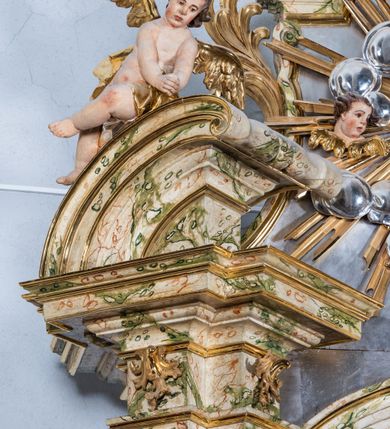 Zdjęcie nr 21: Ołtarz drewniany, prostopadłościenny z kamienną mensą, z kamiennym portatylem. Antepedium z prostokątną płyciną ujętą marmoryzowaną ramą ze złoconym karbowanym profilem. W polu przedstawienie świętej z aniołkiem podającym jej kosz kwiatów, flankowany akantową wicią akantową przeplataną z roślinną, na jasnoniebieskim tle, z datą „1754”. Nastawa ołtarzowa architektoniczna, jednoosiowa, jednokondygnacyjna ze zwieńczeniem na dwustrefowym cokole.  Retabulum flankowane parą opilastrowanych filarów, które dźwigają imposty oraz fragmenty przerwanego półkolistego przyczółka z siedzącymi puttami. Na tle filarów, na konsolach ustawione 2 figury św. Demetriusza i św. Selencjusza. Trzony pilastrów dekorowane zwisami kwiatowymi. W Polu środkowym wnęka w formie stojącego prostokąta zamkniętego łukiem segmentowym nadwieszonego z uskokiem ujęta profilowaną ramą, dekorowaną ornamentem roślinnym, z obrazem św. Heleny. Wnęka od dołu i góry flankowana ornamentem roślinnym i roccailem. Kondygnacja flankowana uszami utworzonymi z roccailu. Zwieńczenie w formie zbliżonej do trapezu o wklęsłych bokach zamknięte fragmentem gzymsu, wyłamanego na kształt łuku segmentowego nadwieszonego, z kartuszem z ornamentem roccailowym. W polu gorejące serce w otoku z obłoków i uskrzydlonych główek anielskich, w glorii promienistej.  Struktura polichromowana w sposób imitujący marmoryzację w kolorze beżowo-zielonym. Ornamentyka i profile złocone, detal i zwieńczenie srebrzone.