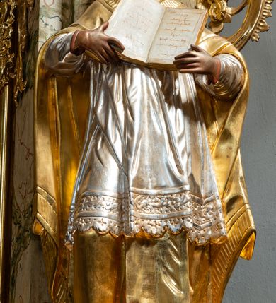 Zdjęcie nr 28: Ołtarz drewniany, prostopadłościenny z kamienną mensą, z kamiennym portatylem. Antependium z prostokątną płyciną ujętą marmoryzowaną ramą ze złoconym karbowanym profilem. W polu medalion w formie stojącego owalu z przedstawieniem zakonnika z dzieciątkiem, flankowany akantową wicią akantową przeplataną z roślinną, na jasnoniebieskim tle. Nastawa ołtarzowa architektoniczna, jednoosiowa, jednokondygnacyjna ze zwieńczeniem na dwustrefowym cokole.  Retabulum flankowane parą opilastrowanych filarów, które dźwigają imposty oraz fragmenty przerwanego półkolistego przyczółka z siedzącymi puttami. Na tle filarów, na konsolach ustawione 2 figury papieża i biskupa. Trzony pilastrów dekorowane zwisami kwiatowymi. W Polu środkowym wnęka w formie stojącego prostokąta zamkniętego łukiem segmentowym nadwieszonego z uskokiem ujęta profilowaną ramą, dekorowaną ornamentem roślinnym, z obrazem świętego Marka. Wnęka od dołu i góry flankowana ornamentem roślinnym i roccailem. Kondygnacja flankowana uszami utworzonymi z roccailu. Zwieńczenie w formie zbliżonej do trapezu o wklęsłych bokach zamknięte fragmentem gzymsu, wyłamanego na kształt łuku segmentowego nadwieszonego, z kartuszem z ornamentem roccailowym. W polu gorejące serce w otoku z obłoków i uskrzydlonych główek anielskich, w glorii promienistej.  Struktura polichromowana w sposób imitujący marmoryzację w kolorze beżowo-zielonym. Ornamentyka i profile złocone, detal i zwieńczenie srebrzone.