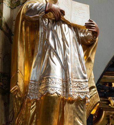 Zdjęcie nr 24: Ołtarz drewniany, prostopadłościenny z kamienną mensą, z kamiennym portatylem. Antependium z prostokątną płyciną ujętą marmoryzowaną ramą ze złoconym karbowanym profilem. W polu medalion w formie stojącego owalu z przedstawieniem zakonnika z dzieciątkiem, flankowany akantową wicią akantową przeplataną z roślinną, na jasnoniebieskim tle. Nastawa ołtarzowa architektoniczna, jednoosiowa, jednokondygnacyjna ze zwieńczeniem na dwustrefowym cokole.  Retabulum flankowane parą opilastrowanych filarów, które dźwigają imposty oraz fragmenty przerwanego półkolistego przyczółka z siedzącymi puttami. Na tle filarów, na konsolach ustawione 2 figury papieża i biskupa. Trzony pilastrów dekorowane zwisami kwiatowymi. W Polu środkowym wnęka w formie stojącego prostokąta zamkniętego łukiem segmentowym nadwieszonego z uskokiem ujęta profilowaną ramą, dekorowaną ornamentem roślinnym, z obrazem świętego Marka. Wnęka od dołu i góry flankowana ornamentem roślinnym i roccailem. Kondygnacja flankowana uszami utworzonymi z roccailu. Zwieńczenie w formie zbliżonej do trapezu o wklęsłych bokach zamknięte fragmentem gzymsu, wyłamanego na kształt łuku segmentowego nadwieszonego, z kartuszem z ornamentem roccailowym. W polu gorejące serce w otoku z obłoków i uskrzydlonych główek anielskich, w glorii promienistej.  Struktura polichromowana w sposób imitujący marmoryzację w kolorze beżowo-zielonym. Ornamentyka i profile złocone, detal i zwieńczenie srebrzone.