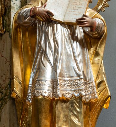 Zdjęcie nr 27: Ołtarz drewniany, prostopadłościenny z kamienną mensą, z kamiennym portatylem. Antependium z prostokątną płyciną ujętą marmoryzowaną ramą ze złoconym karbowanym profilem. W polu medalion w formie stojącego owalu z przedstawieniem zakonnika z dzieciątkiem, flankowany akantową wicią akantową przeplataną z roślinną, na jasnoniebieskim tle. Nastawa ołtarzowa architektoniczna, jednoosiowa, jednokondygnacyjna ze zwieńczeniem na dwustrefowym cokole.  Retabulum flankowane parą opilastrowanych filarów, które dźwigają imposty oraz fragmenty przerwanego półkolistego przyczółka z siedzącymi puttami. Na tle filarów, na konsolach ustawione 2 figury papieża i biskupa. Trzony pilastrów dekorowane zwisami kwiatowymi. W Polu środkowym wnęka w formie stojącego prostokąta zamkniętego łukiem segmentowym nadwieszonego z uskokiem ujęta profilowaną ramą, dekorowaną ornamentem roślinnym, z obrazem świętego Marka. Wnęka od dołu i góry flankowana ornamentem roślinnym i roccailem. Kondygnacja flankowana uszami utworzonymi z roccailu. Zwieńczenie w formie zbliżonej do trapezu o wklęsłych bokach zamknięte fragmentem gzymsu, wyłamanego na kształt łuku segmentowego nadwieszonego, z kartuszem z ornamentem roccailowym. W polu gorejące serce w otoku z obłoków i uskrzydlonych główek anielskich, w glorii promienistej.  Struktura polichromowana w sposób imitujący marmoryzację w kolorze beżowo-zielonym. Ornamentyka i profile złocone, detal i zwieńczenie srebrzone.