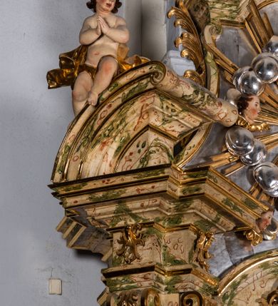 Zdjęcie nr 12: Ołtarz drewniany, prostopadłościenny z kamienną mensą, z kamiennym portatylem. Antependium z prostokątną płyciną ujętą marmoryzowaną ramą ze złoconym karbowanym profilem. W polu medalion w formie stojącego owalu z przedstawieniem zakonnika z dzieciątkiem, flankowany akantową wicią akantową przeplataną z roślinną, na jasnoniebieskim tle. Nastawa ołtarzowa architektoniczna, jednoosiowa, jednokondygnacyjna ze zwieńczeniem na dwustrefowym cokole.  Retabulum flankowane parą opilastrowanych filarów, które dźwigają imposty oraz fragmenty przerwanego półkolistego przyczółka z siedzącymi puttami. Na tle filarów, na konsolach ustawione 2 figury papieża i biskupa. Trzony pilastrów dekorowane zwisami kwiatowymi. W Polu środkowym wnęka w formie stojącego prostokąta zamkniętego łukiem segmentowym nadwieszonego z uskokiem ujęta profilowaną ramą, dekorowaną ornamentem roślinnym, z obrazem świętego Marka. Wnęka od dołu i góry flankowana ornamentem roślinnym i roccailem. Kondygnacja flankowana uszami utworzonymi z roccailu. Zwieńczenie w formie zbliżonej do trapezu o wklęsłych bokach zamknięte fragmentem gzymsu, wyłamanego na kształt łuku segmentowego nadwieszonego, z kartuszem z ornamentem roccailowym. W polu gorejące serce w otoku z obłoków i uskrzydlonych główek anielskich, w glorii promienistej.  Struktura polichromowana w sposób imitujący marmoryzację w kolorze beżowo-zielonym. Ornamentyka i profile złocone, detal i zwieńczenie srebrzone.