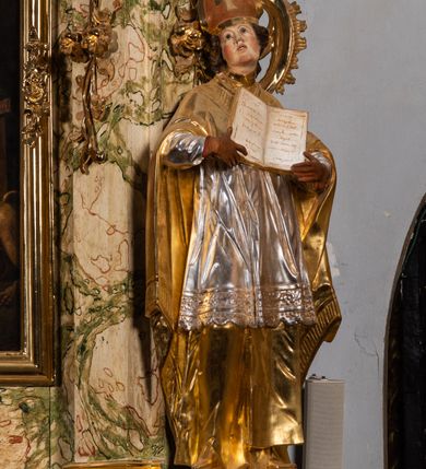 Zdjęcie nr 17: Ołtarz drewniany, prostopadłościenny z kamienną mensą, z kamiennym portatylem. Antependium z prostokątną płyciną ujętą marmoryzowaną ramą ze złoconym karbowanym profilem. W polu medalion w formie stojącego owalu z przedstawieniem zakonnika z dzieciątkiem, flankowany akantową wicią akantową przeplataną z roślinną, na jasnoniebieskim tle. Nastawa ołtarzowa architektoniczna, jednoosiowa, jednokondygnacyjna ze zwieńczeniem na dwustrefowym cokole.  Retabulum flankowane parą opilastrowanych filarów, które dźwigają imposty oraz fragmenty przerwanego półkolistego przyczółka z siedzącymi puttami. Na tle filarów, na konsolach ustawione 2 figury papieża i biskupa. Trzony pilastrów dekorowane zwisami kwiatowymi. W Polu środkowym wnęka w formie stojącego prostokąta zamkniętego łukiem segmentowym nadwieszonego z uskokiem ujęta profilowaną ramą, dekorowaną ornamentem roślinnym, z obrazem świętego Marka. Wnęka od dołu i góry flankowana ornamentem roślinnym i roccailem. Kondygnacja flankowana uszami utworzonymi z roccailu. Zwieńczenie w formie zbliżonej do trapezu o wklęsłych bokach zamknięte fragmentem gzymsu, wyłamanego na kształt łuku segmentowego nadwieszonego, z kartuszem z ornamentem roccailowym. W polu gorejące serce w otoku z obłoków i uskrzydlonych główek anielskich, w glorii promienistej.  Struktura polichromowana w sposób imitujący marmoryzację w kolorze beżowo-zielonym. Ornamentyka i profile złocone, detal i zwieńczenie srebrzone.