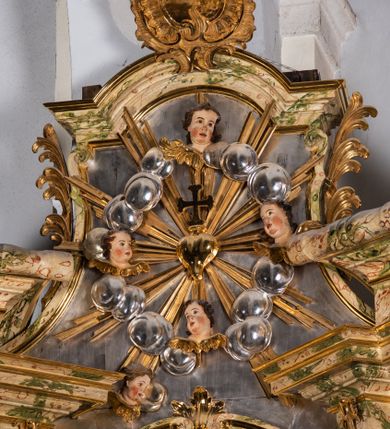 Zdjęcie nr 18: Ołtarz drewniany, prostopadłościenny z kamienną mensą, z kamiennym portatylem. Antependium z prostokątną płyciną ujętą marmoryzowaną ramą ze złoconym karbowanym profilem. W polu medalion w formie stojącego owalu z przedstawieniem zakonnika z dzieciątkiem, flankowany akantową wicią akantową przeplataną z roślinną, na jasnoniebieskim tle. Nastawa ołtarzowa architektoniczna, jednoosiowa, jednokondygnacyjna ze zwieńczeniem na dwustrefowym cokole.  Retabulum flankowane parą opilastrowanych filarów, które dźwigają imposty oraz fragmenty przerwanego półkolistego przyczółka z siedzącymi puttami. Na tle filarów, na konsolach ustawione 2 figury papieża i biskupa. Trzony pilastrów dekorowane zwisami kwiatowymi. W Polu środkowym wnęka w formie stojącego prostokąta zamkniętego łukiem segmentowym nadwieszonego z uskokiem ujęta profilowaną ramą, dekorowaną ornamentem roślinnym, z obrazem świętego Marka. Wnęka od dołu i góry flankowana ornamentem roślinnym i roccailem. Kondygnacja flankowana uszami utworzonymi z roccailu. Zwieńczenie w formie zbliżonej do trapezu o wklęsłych bokach zamknięte fragmentem gzymsu, wyłamanego na kształt łuku segmentowego nadwieszonego, z kartuszem z ornamentem roccailowym. W polu gorejące serce w otoku z obłoków i uskrzydlonych główek anielskich, w glorii promienistej.  Struktura polichromowana w sposób imitujący marmoryzację w kolorze beżowo-zielonym. Ornamentyka i profile złocone, detal i zwieńczenie srebrzone.