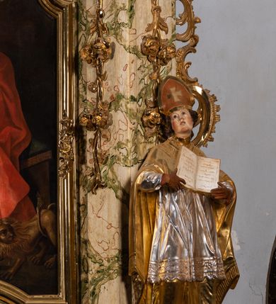 Zdjęcie nr 14: Ołtarz drewniany, prostopadłościenny z kamienną mensą, z kamiennym portatylem. Antependium z prostokątną płyciną ujętą marmoryzowaną ramą ze złoconym karbowanym profilem. W polu medalion w formie stojącego owalu z przedstawieniem zakonnika z dzieciątkiem, flankowany akantową wicią akantową przeplataną z roślinną, na jasnoniebieskim tle. Nastawa ołtarzowa architektoniczna, jednoosiowa, jednokondygnacyjna ze zwieńczeniem na dwustrefowym cokole.  Retabulum flankowane parą opilastrowanych filarów, które dźwigają imposty oraz fragmenty przerwanego półkolistego przyczółka z siedzącymi puttami. Na tle filarów, na konsolach ustawione 2 figury papieża i biskupa. Trzony pilastrów dekorowane zwisami kwiatowymi. W Polu środkowym wnęka w formie stojącego prostokąta zamkniętego łukiem segmentowym nadwieszonego z uskokiem ujęta profilowaną ramą, dekorowaną ornamentem roślinnym, z obrazem świętego Marka. Wnęka od dołu i góry flankowana ornamentem roślinnym i roccailem. Kondygnacja flankowana uszami utworzonymi z roccailu. Zwieńczenie w formie zbliżonej do trapezu o wklęsłych bokach zamknięte fragmentem gzymsu, wyłamanego na kształt łuku segmentowego nadwieszonego, z kartuszem z ornamentem roccailowym. W polu gorejące serce w otoku z obłoków i uskrzydlonych główek anielskich, w glorii promienistej.  Struktura polichromowana w sposób imitujący marmoryzację w kolorze beżowo-zielonym. Ornamentyka i profile złocone, detal i zwieńczenie srebrzone.