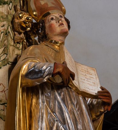 Zdjęcie nr 19: Ołtarz drewniany, prostopadłościenny z kamienną mensą, z kamiennym portatylem. Antependium z prostokątną płyciną ujętą marmoryzowaną ramą ze złoconym karbowanym profilem. W polu medalion w formie stojącego owalu z przedstawieniem zakonnika z dzieciątkiem, flankowany akantową wicią akantową przeplataną z roślinną, na jasnoniebieskim tle. Nastawa ołtarzowa architektoniczna, jednoosiowa, jednokondygnacyjna ze zwieńczeniem na dwustrefowym cokole.  Retabulum flankowane parą opilastrowanych filarów, które dźwigają imposty oraz fragmenty przerwanego półkolistego przyczółka z siedzącymi puttami. Na tle filarów, na konsolach ustawione 2 figury papieża i biskupa. Trzony pilastrów dekorowane zwisami kwiatowymi. W Polu środkowym wnęka w formie stojącego prostokąta zamkniętego łukiem segmentowym nadwieszonego z uskokiem ujęta profilowaną ramą, dekorowaną ornamentem roślinnym, z obrazem świętego Marka. Wnęka od dołu i góry flankowana ornamentem roślinnym i roccailem. Kondygnacja flankowana uszami utworzonymi z roccailu. Zwieńczenie w formie zbliżonej do trapezu o wklęsłych bokach zamknięte fragmentem gzymsu, wyłamanego na kształt łuku segmentowego nadwieszonego, z kartuszem z ornamentem roccailowym. W polu gorejące serce w otoku z obłoków i uskrzydlonych główek anielskich, w glorii promienistej.  Struktura polichromowana w sposób imitujący marmoryzację w kolorze beżowo-zielonym. Ornamentyka i profile złocone, detal i zwieńczenie srebrzone.