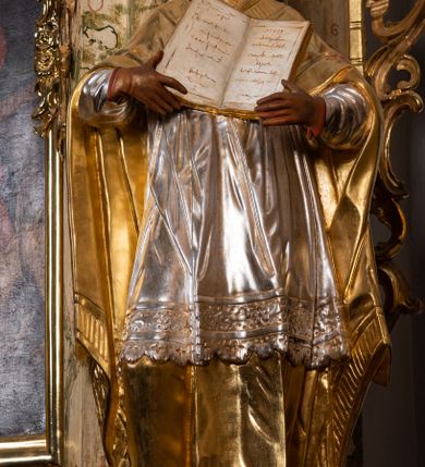 Zdjęcie nr 20: Ołtarz drewniany, prostopadłościenny z kamienną mensą, z kamiennym portatylem. Antependium z prostokątną płyciną ujętą marmoryzowaną ramą ze złoconym karbowanym profilem. W polu medalion w formie stojącego owalu z przedstawieniem zakonnika z dzieciątkiem, flankowany akantową wicią akantową przeplataną z roślinną, na jasnoniebieskim tle. Nastawa ołtarzowa architektoniczna, jednoosiowa, jednokondygnacyjna ze zwieńczeniem na dwustrefowym cokole.  Retabulum flankowane parą opilastrowanych filarów, które dźwigają imposty oraz fragmenty przerwanego półkolistego przyczółka z siedzącymi puttami. Na tle filarów, na konsolach ustawione 2 figury papieża i biskupa. Trzony pilastrów dekorowane zwisami kwiatowymi. W Polu środkowym wnęka w formie stojącego prostokąta zamkniętego łukiem segmentowym nadwieszonego z uskokiem ujęta profilowaną ramą, dekorowaną ornamentem roślinnym, z obrazem świętego Marka. Wnęka od dołu i góry flankowana ornamentem roślinnym i roccailem. Kondygnacja flankowana uszami utworzonymi z roccailu. Zwieńczenie w formie zbliżonej do trapezu o wklęsłych bokach zamknięte fragmentem gzymsu, wyłamanego na kształt łuku segmentowego nadwieszonego, z kartuszem z ornamentem roccailowym. W polu gorejące serce w otoku z obłoków i uskrzydlonych główek anielskich, w glorii promienistej.  Struktura polichromowana w sposób imitujący marmoryzację w kolorze beżowo-zielonym. Ornamentyka i profile złocone, detal i zwieńczenie srebrzone.