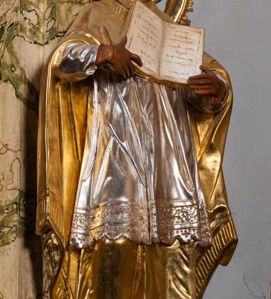 Zdjęcie nr 21: Ołtarz drewniany, prostopadłościenny z kamienną mensą, z kamiennym portatylem. Antependium z prostokątną płyciną ujętą marmoryzowaną ramą ze złoconym karbowanym profilem. W polu medalion w formie stojącego owalu z przedstawieniem zakonnika z dzieciątkiem, flankowany akantową wicią akantową przeplataną z roślinną, na jasnoniebieskim tle. Nastawa ołtarzowa architektoniczna, jednoosiowa, jednokondygnacyjna ze zwieńczeniem na dwustrefowym cokole.  Retabulum flankowane parą opilastrowanych filarów, które dźwigają imposty oraz fragmenty przerwanego półkolistego przyczółka z siedzącymi puttami. Na tle filarów, na konsolach ustawione 2 figury papieża i biskupa. Trzony pilastrów dekorowane zwisami kwiatowymi. W Polu środkowym wnęka w formie stojącego prostokąta zamkniętego łukiem segmentowym nadwieszonego z uskokiem ujęta profilowaną ramą, dekorowaną ornamentem roślinnym, z obrazem świętego Marka. Wnęka od dołu i góry flankowana ornamentem roślinnym i roccailem. Kondygnacja flankowana uszami utworzonymi z roccailu. Zwieńczenie w formie zbliżonej do trapezu o wklęsłych bokach zamknięte fragmentem gzymsu, wyłamanego na kształt łuku segmentowego nadwieszonego, z kartuszem z ornamentem roccailowym. W polu gorejące serce w otoku z obłoków i uskrzydlonych główek anielskich, w glorii promienistej.  Struktura polichromowana w sposób imitujący marmoryzację w kolorze beżowo-zielonym. Ornamentyka i profile złocone, detal i zwieńczenie srebrzone.