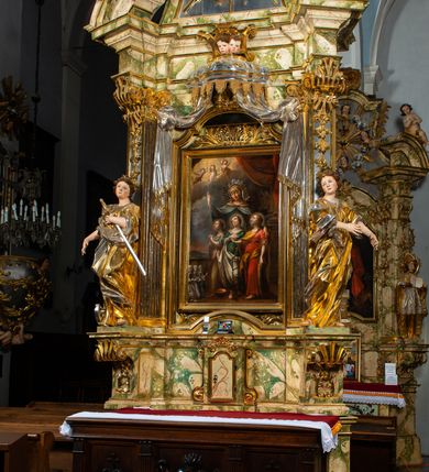 Zdjęcie nr 2: Ołtarz drewniany, prostopadłościenny z kamienną mensą, z kamiennym portatylem. Antepedium drewniane podzielone na trzy płyciny za pomocą pilastrów: w środkowej krzyż, kotwica i gorejące serce, w bocznych gorejące serce w koronie cierniowej i wieńcu z róż. Nastawa ołtarzowa architektoniczna, jednoosiowa, jednokondygnacyjna ze zwieńczeniem na cokole.  Retabulum flankowane parą zdwojonych pilastrów zakończonych konsolami,  które dźwigają pełne belkowanie oraz fragmenty przerwanego półkolistego przyczółka z siedzącymi puttami. Na tle pilastrów, na konsolach ustawione 2 figury: św. Katarzyny oraz Barbary. Trzony pilastrów dekorowane kampanulami. W Polu środkowym wnęka w formie stojącego prostokąta zamkniętego łukiem segmentowym nadwieszonego z uskokiem ujęta profilowaną ramą, z obrazem świętej Zofii z córkami, w osobnej ramie. Nad wnęką baldachim dekorowany lambrekinem, z podwieszoną tkaniną po dwóch stronach, lamowaną frędzlą. Nam baldachimem kartusz z uskrzydlonymi główkami anielskimi i zwieńczony koroną. Zwieńczenie w formie zbliżonej do trapezu o wklęsłych bokach zamknięte falistym gzymsem, dekorowanym uskrzydloną główką anielską, ujętą wolutami na tle muszli, z podwieszonymi kampanulami. W polu gołębica w otoku z obłoków i uskrzydlonych główek anielskich, w glorii promienistej.  Struktura polichromowana w sposób imitujący marmoryzację w kolorze beżowo-zielonym. Ornamentyka i profile złocone, detal i zwieńczenie srebrzone.