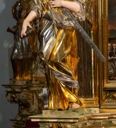 Zdjęcie nr 5: Ołtarz drewniany, prostopadłościenny z kamienną mensą, z kamiennym portatylem. Antepedium drewniane podzielone na trzy płyciny za pomocą pilastrów: w środkowej krzyż, kotwica i gorejące serce, w bocznych gorejące serce w koronie cierniowej i wieńcu z róż. Nastawa ołtarzowa architektoniczna, jednoosiowa, jednokondygnacyjna ze zwieńczeniem na cokole.  Retabulum flankowane parą zdwojonych pilastrów zakończonych konsolami,  które dźwigają pełne belkowanie oraz fragmenty przerwanego półkolistego przyczółka z siedzącymi puttami. Na tle pilastrów, na konsolach ustawione 2 figury: św. Katarzyny oraz Barbary. Trzony pilastrów dekorowane kampanulami. W Polu środkowym wnęka w formie stojącego prostokąta zamkniętego łukiem segmentowym nadwieszonego z uskokiem ujęta profilowaną ramą, z obrazem świętej Zofii z córkami, w osobnej ramie. Nad wnęką baldachim dekorowany lambrekinem, z podwieszoną tkaniną po dwóch stronach, lamowaną frędzlą. Nam baldachimem kartusz z uskrzydlonymi główkami anielskimi i zwieńczony koroną. Zwieńczenie w formie zbliżonej do trapezu o wklęsłych bokach zamknięte falistym gzymsem, dekorowanym uskrzydloną główką anielską, ujętą wolutami na tle muszli, z podwieszonymi kampanulami. W polu gołębica w otoku z obłoków i uskrzydlonych główek anielskich, w glorii promienistej.  Struktura polichromowana w sposób imitujący marmoryzację w kolorze beżowo-zielonym. Ornamentyka i profile złocone, detal i zwieńczenie srebrzone.