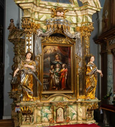 Zdjęcie nr 13: Ołtarz drewniany, prostopadłościenny z kamienną mensą, z kamiennym portatylem. Antepedium drewniane podzielone na trzy płyciny za pomocą pilastrów: w środkowej krzyż, kotwica i gorejące serce, w bocznych gorejące serce w koronie cierniowej i wieńcu z róż. Nastawa ołtarzowa architektoniczna, jednoosiowa, jednokondygnacyjna ze zwieńczeniem na cokole.  Retabulum flankowane parą zdwojonych pilastrów zakończonych konsolami,  które dźwigają pełne belkowanie oraz fragmenty przerwanego półkolistego przyczółka z siedzącymi puttami. Na tle pilastrów, na konsolach ustawione 2 figury: św. Katarzyny oraz Barbary. Trzony pilastrów dekorowane kampanulami. W Polu środkowym wnęka w formie stojącego prostokąta zamkniętego łukiem segmentowym nadwieszonego z uskokiem ujęta profilowaną ramą, z obrazem świętej Zofii z córkami, w osobnej ramie. Nad wnęką baldachim dekorowany lambrekinem, z podwieszoną tkaniną po dwóch stronach, lamowaną frędzlą. Nam baldachimem kartusz z uskrzydlonymi główkami anielskimi i zwieńczony koroną. Zwieńczenie w formie zbliżonej do trapezu o wklęsłych bokach zamknięte falistym gzymsem, dekorowanym uskrzydloną główką anielską, ujętą wolutami na tle muszli, z podwieszonymi kampanulami. W polu gołębica w otoku z obłoków i uskrzydlonych główek anielskich, w glorii promienistej.  Struktura polichromowana w sposób imitujący marmoryzację w kolorze beżowo-zielonym. Ornamentyka i profile złocone, detal i zwieńczenie srebrzone.