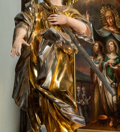 Zdjęcie nr 6: Ołtarz drewniany, prostopadłościenny z kamienną mensą, z kamiennym portatylem. Antepedium drewniane podzielone na trzy płyciny za pomocą pilastrów: w środkowej krzyż, kotwica i gorejące serce, w bocznych gorejące serce w koronie cierniowej i wieńcu z róż. Nastawa ołtarzowa architektoniczna, jednoosiowa, jednokondygnacyjna ze zwieńczeniem na cokole.  Retabulum flankowane parą zdwojonych pilastrów zakończonych konsolami,  które dźwigają pełne belkowanie oraz fragmenty przerwanego półkolistego przyczółka z siedzącymi puttami. Na tle pilastrów, na konsolach ustawione 2 figury: św. Katarzyny oraz Barbary. Trzony pilastrów dekorowane kampanulami. W Polu środkowym wnęka w formie stojącego prostokąta zamkniętego łukiem segmentowym nadwieszonego z uskokiem ujęta profilowaną ramą, z obrazem świętej Zofii z córkami, w osobnej ramie. Nad wnęką baldachim dekorowany lambrekinem, z podwieszoną tkaniną po dwóch stronach, lamowaną frędzlą. Nam baldachimem kartusz z uskrzydlonymi główkami anielskimi i zwieńczony koroną. Zwieńczenie w formie zbliżonej do trapezu o wklęsłych bokach zamknięte falistym gzymsem, dekorowanym uskrzydloną główką anielską, ujętą wolutami na tle muszli, z podwieszonymi kampanulami. W polu gołębica w otoku z obłoków i uskrzydlonych główek anielskich, w glorii promienistej.  Struktura polichromowana w sposób imitujący marmoryzację w kolorze beżowo-zielonym. Ornamentyka i profile złocone, detal i zwieńczenie srebrzone.