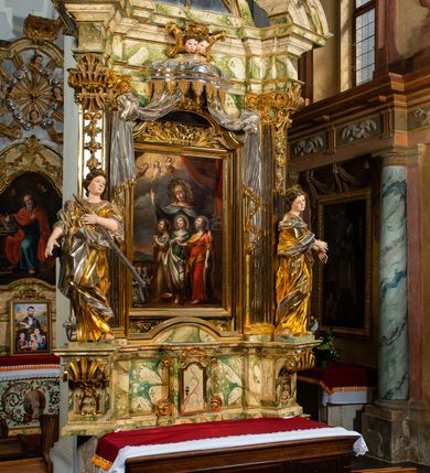 Zdjęcie nr 35: Ołtarz drewniany, prostopadłościenny z kamienną mensą, z kamiennym portatylem. Antepedium drewniane podzielone na trzy płyciny za pomocą pilastrów: w środkowej krzyż, kotwica i gorejące serce, w bocznych gorejące serce w koronie cierniowej i wieńcu z róż. Nastawa ołtarzowa architektoniczna, jednoosiowa, jednokondygnacyjna ze zwieńczeniem na cokole.  Retabulum flankowane parą zdwojonych pilastrów zakończonych konsolami,  które dźwigają pełne belkowanie oraz fragmenty przerwanego półkolistego przyczółka z siedzącymi puttami. Na tle pilastrów, na konsolach ustawione 2 figury: św. Katarzyny oraz Barbary. Trzony pilastrów dekorowane kampanulami. W Polu środkowym wnęka w formie stojącego prostokąta zamkniętego łukiem segmentowym nadwieszonego z uskokiem ujęta profilowaną ramą, z obrazem świętej Zofii z córkami, w osobnej ramie. Nad wnęką baldachim dekorowany lambrekinem, z podwieszoną tkaniną po dwóch stronach, lamowaną frędzlą. Nam baldachimem kartusz z uskrzydlonymi główkami anielskimi i zwieńczony koroną. Zwieńczenie w formie zbliżonej do trapezu o wklęsłych bokach zamknięte falistym gzymsem, dekorowanym uskrzydloną główką anielską, ujętą wolutami na tle muszli, z podwieszonymi kampanulami. W polu gołębica w otoku z obłoków i uskrzydlonych główek anielskich, w glorii promienistej.  Struktura polichromowana w sposób imitujący marmoryzację w kolorze beżowo-zielonym. Ornamentyka i profile złocone, detal i zwieńczenie srebrzone.