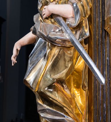 Zdjęcie nr 8: Ołtarz drewniany, prostopadłościenny z kamienną mensą, z kamiennym portatylem. Antepedium drewniane podzielone na trzy płyciny za pomocą pilastrów: w środkowej krzyż, kotwica i gorejące serce, w bocznych gorejące serce w koronie cierniowej i wieńcu z róż. Nastawa ołtarzowa architektoniczna, jednoosiowa, jednokondygnacyjna ze zwieńczeniem na cokole.  Retabulum flankowane parą zdwojonych pilastrów zakończonych konsolami,  które dźwigają pełne belkowanie oraz fragmenty przerwanego półkolistego przyczółka z siedzącymi puttami. Na tle pilastrów, na konsolach ustawione 2 figury: św. Katarzyny oraz Barbary. Trzony pilastrów dekorowane kampanulami. W Polu środkowym wnęka w formie stojącego prostokąta zamkniętego łukiem segmentowym nadwieszonego z uskokiem ujęta profilowaną ramą, z obrazem świętej Zofii z córkami, w osobnej ramie. Nad wnęką baldachim dekorowany lambrekinem, z podwieszoną tkaniną po dwóch stronach, lamowaną frędzlą. Nam baldachimem kartusz z uskrzydlonymi główkami anielskimi i zwieńczony koroną. Zwieńczenie w formie zbliżonej do trapezu o wklęsłych bokach zamknięte falistym gzymsem, dekorowanym uskrzydloną główką anielską, ujętą wolutami na tle muszli, z podwieszonymi kampanulami. W polu gołębica w otoku z obłoków i uskrzydlonych główek anielskich, w glorii promienistej.  Struktura polichromowana w sposób imitujący marmoryzację w kolorze beżowo-zielonym. Ornamentyka i profile złocone, detal i zwieńczenie srebrzone.