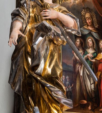 Zdjęcie nr 12: Ołtarz drewniany, prostopadłościenny z kamienną mensą, z kamiennym portatylem. Antepedium drewniane podzielone na trzy płyciny za pomocą pilastrów: w środkowej krzyż, kotwica i gorejące serce, w bocznych gorejące serce w koronie cierniowej i wieńcu z róż. Nastawa ołtarzowa architektoniczna, jednoosiowa, jednokondygnacyjna ze zwieńczeniem na cokole.  Retabulum flankowane parą zdwojonych pilastrów zakończonych konsolami,  które dźwigają pełne belkowanie oraz fragmenty przerwanego półkolistego przyczółka z siedzącymi puttami. Na tle pilastrów, na konsolach ustawione 2 figury: św. Katarzyny oraz Barbary. Trzony pilastrów dekorowane kampanulami. W Polu środkowym wnęka w formie stojącego prostokąta zamkniętego łukiem segmentowym nadwieszonego z uskokiem ujęta profilowaną ramą, z obrazem świętej Zofii z córkami, w osobnej ramie. Nad wnęką baldachim dekorowany lambrekinem, z podwieszoną tkaniną po dwóch stronach, lamowaną frędzlą. Nam baldachimem kartusz z uskrzydlonymi główkami anielskimi i zwieńczony koroną. Zwieńczenie w formie zbliżonej do trapezu o wklęsłych bokach zamknięte falistym gzymsem, dekorowanym uskrzydloną główką anielską, ujętą wolutami na tle muszli, z podwieszonymi kampanulami. W polu gołębica w otoku z obłoków i uskrzydlonych główek anielskich, w glorii promienistej.  Struktura polichromowana w sposób imitujący marmoryzację w kolorze beżowo-zielonym. Ornamentyka i profile złocone, detal i zwieńczenie srebrzone.