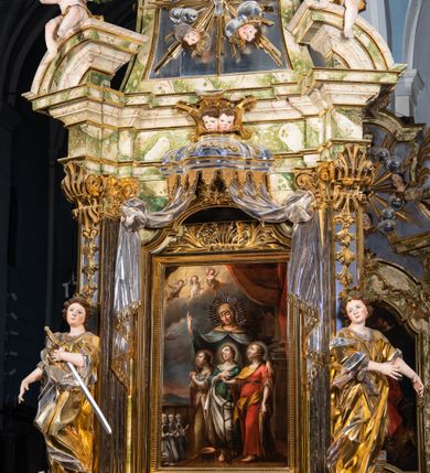 Zdjęcie nr 24: Ołtarz drewniany, prostopadłościenny z kamienną mensą, z kamiennym portatylem. Antepedium drewniane podzielone na trzy płyciny za pomocą pilastrów: w środkowej krzyż, kotwica i gorejące serce, w bocznych gorejące serce w koronie cierniowej i wieńcu z róż. Nastawa ołtarzowa architektoniczna, jednoosiowa, jednokondygnacyjna ze zwieńczeniem na cokole.  Retabulum flankowane parą zdwojonych pilastrów zakończonych konsolami,  które dźwigają pełne belkowanie oraz fragmenty przerwanego półkolistego przyczółka z siedzącymi puttami. Na tle pilastrów, na konsolach ustawione 2 figury: św. Katarzyny oraz Barbary. Trzony pilastrów dekorowane kampanulami. W Polu środkowym wnęka w formie stojącego prostokąta zamkniętego łukiem segmentowym nadwieszonego z uskokiem ujęta profilowaną ramą, z obrazem świętej Zofii z córkami, w osobnej ramie. Nad wnęką baldachim dekorowany lambrekinem, z podwieszoną tkaniną po dwóch stronach, lamowaną frędzlą. Nam baldachimem kartusz z uskrzydlonymi główkami anielskimi i zwieńczony koroną. Zwieńczenie w formie zbliżonej do trapezu o wklęsłych bokach zamknięte falistym gzymsem, dekorowanym uskrzydloną główką anielską, ujętą wolutami na tle muszli, z podwieszonymi kampanulami. W polu gołębica w otoku z obłoków i uskrzydlonych główek anielskich, w glorii promienistej.  Struktura polichromowana w sposób imitujący marmoryzację w kolorze beżowo-zielonym. Ornamentyka i profile złocone, detal i zwieńczenie srebrzone.