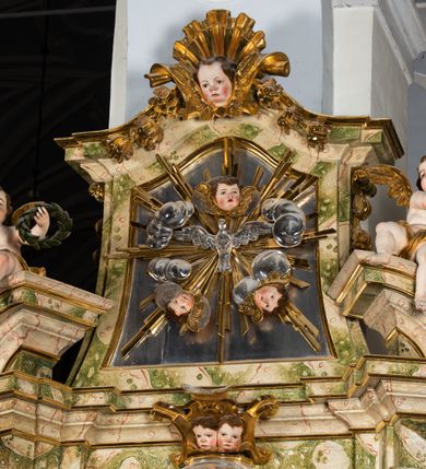 Zdjęcie nr 43: Ołtarz drewniany, prostopadłościenny z kamienną mensą, z kamiennym portatylem. Antepedium drewniane podzielone na trzy płyciny za pomocą pilastrów: w środkowej krzyż, kotwica i gorejące serce, w bocznych gorejące serce w koronie cierniowej i wieńcu z róż. Nastawa ołtarzowa architektoniczna, jednoosiowa, jednokondygnacyjna ze zwieńczeniem na cokole.  Retabulum flankowane parą zdwojonych pilastrów zakończonych konsolami,  które dźwigają pełne belkowanie oraz fragmenty przerwanego półkolistego przyczółka z siedzącymi puttami. Na tle pilastrów, na konsolach ustawione 2 figury: św. Katarzyny oraz Barbary. Trzony pilastrów dekorowane kampanulami. W Polu środkowym wnęka w formie stojącego prostokąta zamkniętego łukiem segmentowym nadwieszonego z uskokiem ujęta profilowaną ramą, z obrazem świętej Zofii z córkami, w osobnej ramie. Nad wnęką baldachim dekorowany lambrekinem, z podwieszoną tkaniną po dwóch stronach, lamowaną frędzlą. Nam baldachimem kartusz z uskrzydlonymi główkami anielskimi i zwieńczony koroną. Zwieńczenie w formie zbliżonej do trapezu o wklęsłych bokach zamknięte falistym gzymsem, dekorowanym uskrzydloną główką anielską, ujętą wolutami na tle muszli, z podwieszonymi kampanulami. W polu gołębica w otoku z obłoków i uskrzydlonych główek anielskich, w glorii promienistej.  Struktura polichromowana w sposób imitujący marmoryzację w kolorze beżowo-zielonym. Ornamentyka i profile złocone, detal i zwieńczenie srebrzone.