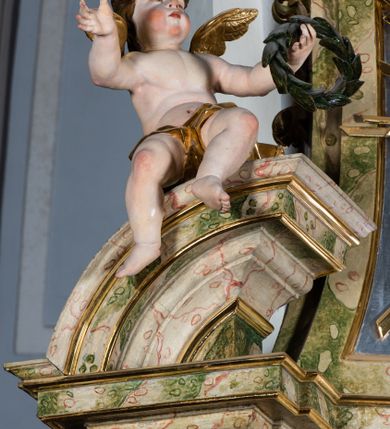 Zdjęcie nr 47: Ołtarz drewniany, prostopadłościenny z kamienną mensą, z kamiennym portatylem. Antepedium drewniane podzielone na trzy płyciny za pomocą pilastrów: w środkowej krzyż, kotwica i gorejące serce, w bocznych gorejące serce w koronie cierniowej i wieńcu z róż. Nastawa ołtarzowa architektoniczna, jednoosiowa, jednokondygnacyjna ze zwieńczeniem na cokole.  Retabulum flankowane parą zdwojonych pilastrów zakończonych konsolami,  które dźwigają pełne belkowanie oraz fragmenty przerwanego półkolistego przyczółka z siedzącymi puttami. Na tle pilastrów, na konsolach ustawione 2 figury: św. Katarzyny oraz Barbary. Trzony pilastrów dekorowane kampanulami. W Polu środkowym wnęka w formie stojącego prostokąta zamkniętego łukiem segmentowym nadwieszonego z uskokiem ujęta profilowaną ramą, z obrazem świętej Zofii z córkami, w osobnej ramie. Nad wnęką baldachim dekorowany lambrekinem, z podwieszoną tkaniną po dwóch stronach, lamowaną frędzlą. Nam baldachimem kartusz z uskrzydlonymi główkami anielskimi i zwieńczony koroną. Zwieńczenie w formie zbliżonej do trapezu o wklęsłych bokach zamknięte falistym gzymsem, dekorowanym uskrzydloną główką anielską, ujętą wolutami na tle muszli, z podwieszonymi kampanulami. W polu gołębica w otoku z obłoków i uskrzydlonych główek anielskich, w glorii promienistej.  Struktura polichromowana w sposób imitujący marmoryzację w kolorze beżowo-zielonym. Ornamentyka i profile złocone, detal i zwieńczenie srebrzone.