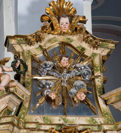 Zdjęcie nr 48: Ołtarz drewniany, prostopadłościenny z kamienną mensą, z kamiennym portatylem. Antepedium drewniane podzielone na trzy płyciny za pomocą pilastrów: w środkowej krzyż, kotwica i gorejące serce, w bocznych gorejące serce w koronie cierniowej i wieńcu z róż. Nastawa ołtarzowa architektoniczna, jednoosiowa, jednokondygnacyjna ze zwieńczeniem na cokole.  Retabulum flankowane parą zdwojonych pilastrów zakończonych konsolami,  które dźwigają pełne belkowanie oraz fragmenty przerwanego półkolistego przyczółka z siedzącymi puttami. Na tle pilastrów, na konsolach ustawione 2 figury: św. Katarzyny oraz Barbary. Trzony pilastrów dekorowane kampanulami. W Polu środkowym wnęka w formie stojącego prostokąta zamkniętego łukiem segmentowym nadwieszonego z uskokiem ujęta profilowaną ramą, z obrazem świętej Zofii z córkami, w osobnej ramie. Nad wnęką baldachim dekorowany lambrekinem, z podwieszoną tkaniną po dwóch stronach, lamowaną frędzlą. Nam baldachimem kartusz z uskrzydlonymi główkami anielskimi i zwieńczony koroną. Zwieńczenie w formie zbliżonej do trapezu o wklęsłych bokach zamknięte falistym gzymsem, dekorowanym uskrzydloną główką anielską, ujętą wolutami na tle muszli, z podwieszonymi kampanulami. W polu gołębica w otoku z obłoków i uskrzydlonych główek anielskich, w glorii promienistej.  Struktura polichromowana w sposób imitujący marmoryzację w kolorze beżowo-zielonym. Ornamentyka i profile złocone, detal i zwieńczenie srebrzone.