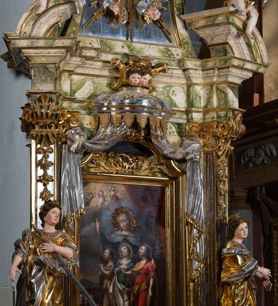 Zdjęcie nr 50: Ołtarz drewniany, prostopadłościenny z kamienną mensą, z kamiennym portatylem. Antepedium drewniane podzielone na trzy płyciny za pomocą pilastrów: w środkowej krzyż, kotwica i gorejące serce, w bocznych gorejące serce w koronie cierniowej i wieńcu z róż. Nastawa ołtarzowa architektoniczna, jednoosiowa, jednokondygnacyjna ze zwieńczeniem na cokole.  Retabulum flankowane parą zdwojonych pilastrów zakończonych konsolami,  które dźwigają pełne belkowanie oraz fragmenty przerwanego półkolistego przyczółka z siedzącymi puttami. Na tle pilastrów, na konsolach ustawione 2 figury: św. Katarzyny oraz Barbary. Trzony pilastrów dekorowane kampanulami. W Polu środkowym wnęka w formie stojącego prostokąta zamkniętego łukiem segmentowym nadwieszonego z uskokiem ujęta profilowaną ramą, z obrazem świętej Zofii z córkami, w osobnej ramie. Nad wnęką baldachim dekorowany lambrekinem, z podwieszoną tkaniną po dwóch stronach, lamowaną frędzlą. Nam baldachimem kartusz z uskrzydlonymi główkami anielskimi i zwieńczony koroną. Zwieńczenie w formie zbliżonej do trapezu o wklęsłych bokach zamknięte falistym gzymsem, dekorowanym uskrzydloną główką anielską, ujętą wolutami na tle muszli, z podwieszonymi kampanulami. W polu gołębica w otoku z obłoków i uskrzydlonych główek anielskich, w glorii promienistej.  Struktura polichromowana w sposób imitujący marmoryzację w kolorze beżowo-zielonym. Ornamentyka i profile złocone, detal i zwieńczenie srebrzone.
