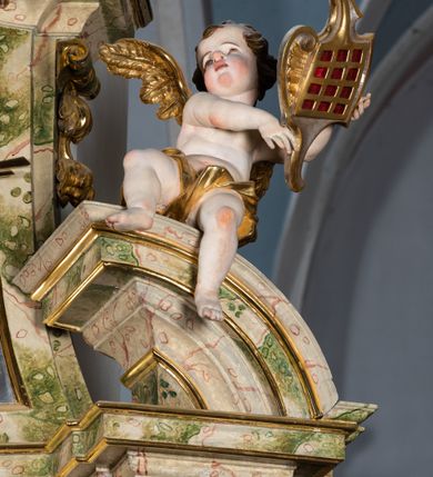 Zdjęcie nr 56: Ołtarz drewniany, prostopadłościenny z kamienną mensą, z kamiennym portatylem. Antepedium drewniane podzielone na trzy płyciny za pomocą pilastrów: w środkowej krzyż, kotwica i gorejące serce, w bocznych gorejące serce w koronie cierniowej i wieńcu z róż. Nastawa ołtarzowa architektoniczna, jednoosiowa, jednokondygnacyjna ze zwieńczeniem na cokole.  Retabulum flankowane parą zdwojonych pilastrów zakończonych konsolami,  które dźwigają pełne belkowanie oraz fragmenty przerwanego półkolistego przyczółka z siedzącymi puttami. Na tle pilastrów, na konsolach ustawione 2 figury: św. Katarzyny oraz Barbary. Trzony pilastrów dekorowane kampanulami. W Polu środkowym wnęka w formie stojącego prostokąta zamkniętego łukiem segmentowym nadwieszonego z uskokiem ujęta profilowaną ramą, z obrazem świętej Zofii z córkami, w osobnej ramie. Nad wnęką baldachim dekorowany lambrekinem, z podwieszoną tkaniną po dwóch stronach, lamowaną frędzlą. Nam baldachimem kartusz z uskrzydlonymi główkami anielskimi i zwieńczony koroną. Zwieńczenie w formie zbliżonej do trapezu o wklęsłych bokach zamknięte falistym gzymsem, dekorowanym uskrzydloną główką anielską, ujętą wolutami na tle muszli, z podwieszonymi kampanulami. W polu gołębica w otoku z obłoków i uskrzydlonych główek anielskich, w glorii promienistej.  Struktura polichromowana w sposób imitujący marmoryzację w kolorze beżowo-zielonym. Ornamentyka i profile złocone, detal i zwieńczenie srebrzone.