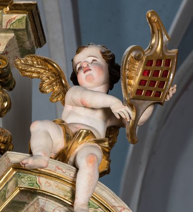 Zdjęcie nr 55: Ołtarz drewniany, prostopadłościenny z kamienną mensą, z kamiennym portatylem. Antepedium drewniane podzielone na trzy płyciny za pomocą pilastrów: w środkowej krzyż, kotwica i gorejące serce, w bocznych gorejące serce w koronie cierniowej i wieńcu z róż. Nastawa ołtarzowa architektoniczna, jednoosiowa, jednokondygnacyjna ze zwieńczeniem na cokole.  Retabulum flankowane parą zdwojonych pilastrów zakończonych konsolami,  które dźwigają pełne belkowanie oraz fragmenty przerwanego półkolistego przyczółka z siedzącymi puttami. Na tle pilastrów, na konsolach ustawione 2 figury: św. Katarzyny oraz Barbary. Trzony pilastrów dekorowane kampanulami. W Polu środkowym wnęka w formie stojącego prostokąta zamkniętego łukiem segmentowym nadwieszonego z uskokiem ujęta profilowaną ramą, z obrazem świętej Zofii z córkami, w osobnej ramie. Nad wnęką baldachim dekorowany lambrekinem, z podwieszoną tkaniną po dwóch stronach, lamowaną frędzlą. Nam baldachimem kartusz z uskrzydlonymi główkami anielskimi i zwieńczony koroną. Zwieńczenie w formie zbliżonej do trapezu o wklęsłych bokach zamknięte falistym gzymsem, dekorowanym uskrzydloną główką anielską, ujętą wolutami na tle muszli, z podwieszonymi kampanulami. W polu gołębica w otoku z obłoków i uskrzydlonych główek anielskich, w glorii promienistej.  Struktura polichromowana w sposób imitujący marmoryzację w kolorze beżowo-zielonym. Ornamentyka i profile złocone, detal i zwieńczenie srebrzone.