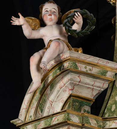 Zdjęcie nr 54: Ołtarz drewniany, prostopadłościenny z kamienną mensą, z kamiennym portatylem. Antepedium drewniane podzielone na trzy płyciny za pomocą pilastrów: w środkowej krzyż, kotwica i gorejące serce, w bocznych gorejące serce w koronie cierniowej i wieńcu z róż. Nastawa ołtarzowa architektoniczna, jednoosiowa, jednokondygnacyjna ze zwieńczeniem na cokole.  Retabulum flankowane parą zdwojonych pilastrów zakończonych konsolami,  które dźwigają pełne belkowanie oraz fragmenty przerwanego półkolistego przyczółka z siedzącymi puttami. Na tle pilastrów, na konsolach ustawione 2 figury: św. Katarzyny oraz Barbary. Trzony pilastrów dekorowane kampanulami. W Polu środkowym wnęka w formie stojącego prostokąta zamkniętego łukiem segmentowym nadwieszonego z uskokiem ujęta profilowaną ramą, z obrazem świętej Zofii z córkami, w osobnej ramie. Nad wnęką baldachim dekorowany lambrekinem, z podwieszoną tkaniną po dwóch stronach, lamowaną frędzlą. Nam baldachimem kartusz z uskrzydlonymi główkami anielskimi i zwieńczony koroną. Zwieńczenie w formie zbliżonej do trapezu o wklęsłych bokach zamknięte falistym gzymsem, dekorowanym uskrzydloną główką anielską, ujętą wolutami na tle muszli, z podwieszonymi kampanulami. W polu gołębica w otoku z obłoków i uskrzydlonych główek anielskich, w glorii promienistej.  Struktura polichromowana w sposób imitujący marmoryzację w kolorze beżowo-zielonym. Ornamentyka i profile złocone, detal i zwieńczenie srebrzone.