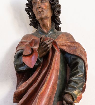 Zdjęcie nr 16: Rzeźba przedstawiająca ukrzyżowanego Chrystusa o ciele ukazanym w delikatnym zwisie ze szczupłymi, wyprężonymi ramionami tworzącymi zarys litery „V”. Głowa Zbawiciela pochylona na prawe ramię z umieszczoną na niej cierniową koroną w formie kołpaka i złoconym nimbem promienistym. Twarz Chrystusa szczupła, oczy zamknięte, nos długi prosty, usta otwarte. Długie, ciemne włosy spływają na prawe ramię długim, skręconym lokiem. Zarost krótki, ciemnobrązowy. Ciało Chrystusa z widoczną raną w prawym boku oddane realistycznie, stopy przebite jednym gwoździem. Wokół bioder udrapowane krótkie, złocone perizonium tworzące płytkie fałdy. U szczytu pionowej belki krzyża titulus w formie banderoli z napisem „INRI”. Krzyż prosty, drewniany w kolorze ciemnobrązowym. Figura w pełni polichromowana, perizonium i nimb złocone.