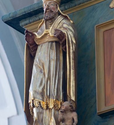 Zdjęcie nr 4: Chór muzyczny konstrukcji drewnianej, wparty na dwóch kamiennych kolumnach o prostych impostowych kapitelach. Balustrada chóru pełna o dekoracji płycinowej (naprzemiennie płyciny owalne, prostokątna i sześcioboczne), zwieńczona profilowanym gzymsem. W dołu ażurowa, wycinana dekoracja. Część środkowa parapetu przełamana i wysunięta do przodu z ustawionymi na niewielkich konsolach polichromowanymi, złoconymi i srebrzonymi figurami: anioła (po środku), św. Wojciecha (?) z lewej i św. Stanisława z prawej. Struktura marmoryzowana w odcieniach zgaszonego niebieskiego, wnętrza płycin w kolorze ceglastej czerwieni. Organy o formie architektonicznej, dziewięcioosiowe z zaakcentowanymi osiami nieparzystymi. Dekorowane złoconym ornamentem akantowym, palmetami, girlandami oraz rocaille&#039;m. Osie trzecia i siódma dodatkowe zwieńczone złoconymi wazonami. Struktura marmoryzowana w odcieniach zgaszonego koloru niebieskiego.