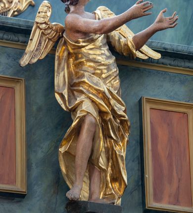 Zdjęcie nr 5: Chór muzyczny konstrukcji drewnianej, wparty na dwóch kamiennych kolumnach o prostych impostowych kapitelach. Balustrada chóru pełna o dekoracji płycinowej (naprzemiennie płyciny owalne, prostokątna i sześcioboczne), zwieńczona profilowanym gzymsem. W dołu ażurowa, wycinana dekoracja. Część środkowa parapetu przełamana i wysunięta do przodu z ustawionymi na niewielkich konsolach polichromowanymi, złoconymi i srebrzonymi figurami: anioła (po środku), św. Wojciecha (?) z lewej i św. Stanisława z prawej. Struktura marmoryzowana w odcieniach zgaszonego niebieskiego, wnętrza płycin w kolorze ceglastej czerwieni. Organy o formie architektonicznej, dziewięcioosiowe z zaakcentowanymi osiami nieparzystymi. Dekorowane złoconym ornamentem akantowym, palmetami, girlandami oraz rocaille&#039;m. Osie trzecia i siódma dodatkowe zwieńczone złoconymi wazonami. Struktura marmoryzowana w odcieniach zgaszonego koloru niebieskiego.