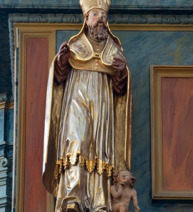 Zdjęcie nr 6: Chór muzyczny konstrukcji drewnianej, wparty na dwóch kamiennych kolumnach o prostych impostowych kapitelach. Balustrada chóru pełna o dekoracji płycinowej (naprzemiennie płyciny owalne, prostokątna i sześcioboczne), zwieńczona profilowanym gzymsem. W dołu ażurowa, wycinana dekoracja. Część środkowa parapetu przełamana i wysunięta do przodu z ustawionymi na niewielkich konsolach polichromowanymi, złoconymi i srebrzonymi figurami: anioła (po środku), św. Wojciecha (?) z lewej i św. Stanisława z prawej. Struktura marmoryzowana w odcieniach zgaszonego niebieskiego, wnętrza płycin w kolorze ceglastej czerwieni. Organy o formie architektonicznej, dziewięcioosiowe z zaakcentowanymi osiami nieparzystymi. Dekorowane złoconym ornamentem akantowym, palmetami, girlandami oraz rocaille&#039;m. Osie trzecia i siódma dodatkowe zwieńczone złoconymi wazonami. Struktura marmoryzowana w odcieniach zgaszonego koloru niebieskiego.