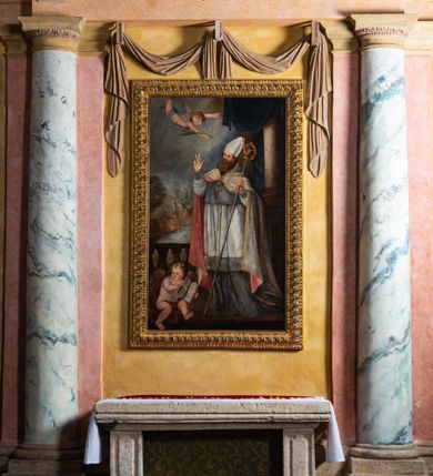 Zdjęcie nr 8: Obraz w kształcie stojącego prostokąta ujęty złoconą ramą dekorowaną motywem plecionki. W centrum kompozycji ukazany stojący, zwrócony w trzech czwartych w prawo św. Erazm. Ukazany jako dojrzały mężczyzna z długą, brązową brodą, ubrany w strój biskupi (alba, rokieta, mucet, kapa, infuła, na szyi pektorał). Święty unosi głowę i prawą rękę ułożoną w geście błogosławieństwa ku górze. W lewym ręku trzyma pastorał. Ponad głową świętego unosi się anioł trzymający palmę męczeństwa. W lewym, dolnym rogu kompozycji przedstawiony siedzący anioł trzymający otwartą księgę z napisem: „S[anctus] Erasmus”. W tle kompozycji, z prawej strony widoczna kolumna z podwieszoną granatową kotarą oraz fragment balustrady (z lewej). Na dalszym planie, w pomniejszonej skali przedstawione sumarycznie postaci na tle rozległego pejzażu.