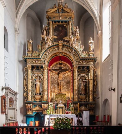 Zdjęcie nr 2: Ołtarz architektoniczny, trójosiowy, dwukondygnacyjny ze zwieńczeniem. Mensa prostopadłościenna, kamienna z drewnianym antepedium w formie leżącego prostokąta z postacią św. Augustyna ujętego wicią suchego akantu z przeplecioną, karbowaną wstążką i bukietami kwiatów. Przedstawienie otoczone profilowaną, ażurową ramą wypełnioną podobną wicią z akantu i kwiatów. Na mensie prostopadłościenne tabernakulum w formie kapliczki. Ściana frontowa z drzwiczkami w kształcie stojącego prostokąta dekorowanego krzyżem łacińskim ujętym wicią roślinną, zwieńczona trójkątnym przyczółkiem. Ścianka ujęta lizenami wypełnionymi wicią akantową podtrzymującymi pełne belkowanie obiegające bryłę, z mocno wysuniętym gzymsem wyłamanym w narożach. Całość zwieńczona czterospadowym dachem dekorowanym łuską. Na dachu baranek Boży leżący na księdze z siedmioma pieczęciami, przytrzymujący chorągiew, ukazany na tle chrystogramu otoczonego glorią promienistą. 
Nastawa na dwudzielnym cokole z półkolistymi bramkami ze zwieńczeniem utworzonym z ornamentu okuciowego ujmującego owalne pola. Osie pierwszej kondygnacji wydzielone kolumnami stojącymi na konsolach dekorowanych z frontu uskrzydlonymi główkami anielskimi powyżej liści akantu, na krawędziach cekinami, a po bokach wicią. Kolumny zostały przedzielone opaską w jednej trzeciej wysokości, dekorowane na całej wysokości wicią roślinną, główkami anielskimi w dolnej partii i imitacją kameryzacji na opaskach oraz w dwóch trzecich wysokości. Kolumny są ustawione na tle pilastrów dekorowanych wicią roślinną i zawieszonymi na niej chustkami. W polu centralnym kondygnacji jest nisza w kształcie stojącego prostokąta zamkniętego łukiem pełnym z postacią ukrzyżowanego Chrystusa na tle widoku Jerozolimy. W osiach bocznych mniejsze, ujęte pilastrami nisze o podobnym kształcie, których konchy wypełnione są muszlą, zwieńczone trójkątnym przyczółkiem przerwanym na cokół. W nich, na dekorowanych wicią i rozetami konsolach ustawiono figury: po lewej stronie św. Piotra, a po prawej św. Pawła. Kondygnacje ujmują ażurowe uszaki utworzone z ornamentu okuciowego, ulistnionych wolut i przewieszonej chustki. Kolumny podtrzymują pełne belkowanie wyniesione w łuk nad polem centralnym. Podłucze dekorowane rozetami, fryz głowami anielskimi i wicią, gzyms m.in. kostkowaniem i liśćmi akantu. Całość spięta kluczem z kartuszem z herbem kanoników regularnych od pokuty (marków). Na wyniesieniu belkowania posadowiono postaci aniołów trzymających narzędzia męki: anioł po lewej włócznię, a anioł po prawej gąbkę. Górna kondygnacja oparta została na schemacie aediculi – prostokątne pole ujęto kolumnami podtrzymującymi pełne belkowanie i trójkątny przyczółek przerwany na środku na cokół, na którym ustawiono rzeźbę  pelikana karmiącego młode własną krwią. Na krawędziach przyczółka dwie leżące postaci. Kondygnacja flankowana postaciami czterech ewangelistów ustawionymi na cokołach. Po lewej stronie św. Marek i św. Jan, po prawej św. Mateusz i św. Łukasz. Struktura polichromowana na kolor ciemnoniebieski; kolumny, profile, detale i ornamenty złocone i srebrzone.
