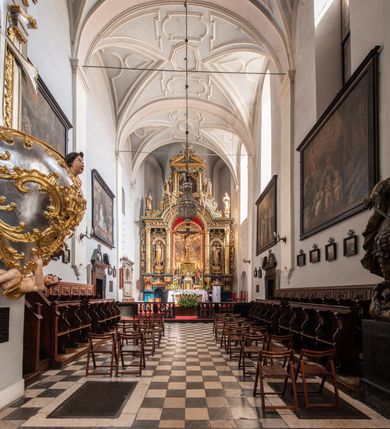 Zdjęcie nr 25: Ołtarz architektoniczny, trójosiowy, dwukondygnacyjny ze zwieńczeniem. Mensa prostopadłościenna, kamienna z drewnianym antepedium w formie leżącego prostokąta z postacią św. Augustyna ujętego wicią suchego akantu z przeplecioną, karbowaną wstążką i bukietami kwiatów. Przedstawienie otoczone profilowaną, ażurową ramą wypełnioną podobną wicią z akantu i kwiatów. Na mensie prostopadłościenne tabernakulum w formie kapliczki. Ściana frontowa z drzwiczkami w kształcie stojącego prostokąta dekorowanego krzyżem łacińskim ujętym wicią roślinną, zwieńczona trójkątnym przyczółkiem. Ścianka ujęta lizenami wypełnionymi wicią akantową podtrzymującymi pełne belkowanie obiegające bryłę, z mocno wysuniętym gzymsem wyłamanym w narożach. Całość zwieńczona czterospadowym dachem dekorowanym łuską. Na dachu baranek Boży leżący na księdze z siedmioma pieczęciami, przytrzymujący chorągiew, ukazany na tle chrystogramu otoczonego glorią promienistą. 
Nastawa na dwudzielnym cokole z półkolistymi bramkami ze zwieńczeniem utworzonym z ornamentu okuciowego ujmującego owalne pola. Osie pierwszej kondygnacji wydzielone kolumnami stojącymi na konsolach dekorowanych z frontu uskrzydlonymi główkami anielskimi powyżej liści akantu, na krawędziach cekinami, a po bokach wicią. Kolumny zostały przedzielone opaską w jednej trzeciej wysokości, dekorowane na całej wysokości wicią roślinną, główkami anielskimi w dolnej partii i imitacją kameryzacji na opaskach oraz w dwóch trzecich wysokości. Kolumny są ustawione na tle pilastrów dekorowanych wicią roślinną i zawieszonymi na niej chustkami. W polu centralnym kondygnacji jest nisza w kształcie stojącego prostokąta zamkniętego łukiem pełnym z postacią ukrzyżowanego Chrystusa na tle widoku Jerozolimy. W osiach bocznych mniejsze, ujęte pilastrami nisze o podobnym kształcie, których konchy wypełnione są muszlą, zwieńczone trójkątnym przyczółkiem przerwanym na cokół. W nich, na dekorowanych wicią i rozetami konsolach ustawiono figury: po lewej stronie św. Piotra, a po prawej św. Pawła. Kondygnacje ujmują ażurowe uszaki utworzone z ornamentu okuciowego, ulistnionych wolut i przewieszonej chustki. Kolumny podtrzymują pełne belkowanie wyniesione w łuk nad polem centralnym. Podłucze dekorowane rozetami, fryz głowami anielskimi i wicią, gzyms m.in. kostkowaniem i liśćmi akantu. Całość spięta kluczem z kartuszem z herbem kanoników regularnych od pokuty (marków). Na wyniesieniu belkowania posadowiono postaci aniołów trzymających narzędzia męki: anioł po lewej włócznię, a anioł po prawej gąbkę. Górna kondygnacja oparta została na schemacie aediculi – prostokątne pole ujęto kolumnami podtrzymującymi pełne belkowanie i trójkątny przyczółek przerwany na środku na cokół, na którym ustawiono rzeźbę  pelikana karmiącego młode własną krwią. Na krawędziach przyczółka dwie leżące postaci. Kondygnacja flankowana postaciami czterech ewangelistów ustawionymi na cokołach. Po lewej stronie św. Marek i św. Jan, po prawej św. Mateusz i św. Łukasz. Struktura polichromowana na kolor ciemnoniebieski; kolumny, profile, detale i ornamenty złocone i srebrzone.
