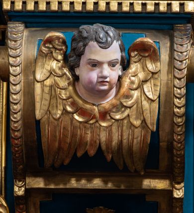 Zdjęcie nr 19: Ołtarz architektoniczny, trójosiowy, dwukondygnacyjny ze zwieńczeniem. Mensa prostopadłościenna, kamienna z drewnianym antepedium w formie leżącego prostokąta z postacią św. Augustyna ujętego wicią suchego akantu z przeplecioną, karbowaną wstążką i bukietami kwiatów. Przedstawienie otoczone profilowaną, ażurową ramą wypełnioną podobną wicią z akantu i kwiatów. Na mensie prostopadłościenne tabernakulum w formie kapliczki. Ściana frontowa z drzwiczkami w kształcie stojącego prostokąta dekorowanego krzyżem łacińskim ujętym wicią roślinną, zwieńczona trójkątnym przyczółkiem. Ścianka ujęta lizenami wypełnionymi wicią akantową podtrzymującymi pełne belkowanie obiegające bryłę, z mocno wysuniętym gzymsem wyłamanym w narożach. Całość zwieńczona czterospadowym dachem dekorowanym łuską. Na dachu baranek Boży leżący na księdze z siedmioma pieczęciami, przytrzymujący chorągiew, ukazany na tle chrystogramu otoczonego glorią promienistą. 
Nastawa na dwudzielnym cokole z półkolistymi bramkami ze zwieńczeniem utworzonym z ornamentu okuciowego ujmującego owalne pola. Osie pierwszej kondygnacji wydzielone kolumnami stojącymi na konsolach dekorowanych z frontu uskrzydlonymi główkami anielskimi powyżej liści akantu, na krawędziach cekinami, a po bokach wicią. Kolumny zostały przedzielone opaską w jednej trzeciej wysokości, dekorowane na całej wysokości wicią roślinną, główkami anielskimi w dolnej partii i imitacją kameryzacji na opaskach oraz w dwóch trzecich wysokości. Kolumny są ustawione na tle pilastrów dekorowanych wicią roślinną i zawieszonymi na niej chustkami. W polu centralnym kondygnacji jest nisza w kształcie stojącego prostokąta zamkniętego łukiem pełnym z postacią ukrzyżowanego Chrystusa na tle widoku Jerozolimy. W osiach bocznych mniejsze, ujęte pilastrami nisze o podobnym kształcie, których konchy wypełnione są muszlą, zwieńczone trójkątnym przyczółkiem przerwanym na cokół. W nich, na dekorowanych wicią i rozetami konsolach ustawiono figury: po lewej stronie św. Piotra, a po prawej św. Pawła. Kondygnacje ujmują ażurowe uszaki utworzone z ornamentu okuciowego, ulistnionych wolut i przewieszonej chustki. Kolumny podtrzymują pełne belkowanie wyniesione w łuk nad polem centralnym. Podłucze dekorowane rozetami, fryz głowami anielskimi i wicią, gzyms m.in. kostkowaniem i liśćmi akantu. Całość spięta kluczem z kartuszem z herbem kanoników regularnych od pokuty (marków). Na wyniesieniu belkowania posadowiono postaci aniołów trzymających narzędzia męki: anioł po lewej włócznię, a anioł po prawej gąbkę. Górna kondygnacja oparta została na schemacie aediculi – prostokątne pole ujęto kolumnami podtrzymującymi pełne belkowanie i trójkątny przyczółek przerwany na środku na cokół, na którym ustawiono rzeźbę  pelikana karmiącego młode własną krwią. Na krawędziach przyczółka dwie leżące postaci. Kondygnacja flankowana postaciami czterech ewangelistów ustawionymi na cokołach. Po lewej stronie św. Marek i św. Jan, po prawej św. Mateusz i św. Łukasz. Struktura polichromowana na kolor ciemnoniebieski; kolumny, profile, detale i ornamenty złocone i srebrzone.
