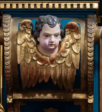 Zdjęcie nr 18: Ołtarz architektoniczny, trójosiowy, dwukondygnacyjny ze zwieńczeniem. Mensa prostopadłościenna, kamienna z drewnianym antepedium w formie leżącego prostokąta z postacią św. Augustyna ujętego wicią suchego akantu z przeplecioną, karbowaną wstążką i bukietami kwiatów. Przedstawienie otoczone profilowaną, ażurową ramą wypełnioną podobną wicią z akantu i kwiatów. Na mensie prostopadłościenne tabernakulum w formie kapliczki. Ściana frontowa z drzwiczkami w kształcie stojącego prostokąta dekorowanego krzyżem łacińskim ujętym wicią roślinną, zwieńczona trójkątnym przyczółkiem. Ścianka ujęta lizenami wypełnionymi wicią akantową podtrzymującymi pełne belkowanie obiegające bryłę, z mocno wysuniętym gzymsem wyłamanym w narożach. Całość zwieńczona czterospadowym dachem dekorowanym łuską. Na dachu baranek Boży leżący na księdze z siedmioma pieczęciami, przytrzymujący chorągiew, ukazany na tle chrystogramu otoczonego glorią promienistą. 
Nastawa na dwudzielnym cokole z półkolistymi bramkami ze zwieńczeniem utworzonym z ornamentu okuciowego ujmującego owalne pola. Osie pierwszej kondygnacji wydzielone kolumnami stojącymi na konsolach dekorowanych z frontu uskrzydlonymi główkami anielskimi powyżej liści akantu, na krawędziach cekinami, a po bokach wicią. Kolumny zostały przedzielone opaską w jednej trzeciej wysokości, dekorowane na całej wysokości wicią roślinną, główkami anielskimi w dolnej partii i imitacją kameryzacji na opaskach oraz w dwóch trzecich wysokości. Kolumny są ustawione na tle pilastrów dekorowanych wicią roślinną i zawieszonymi na niej chustkami. W polu centralnym kondygnacji jest nisza w kształcie stojącego prostokąta zamkniętego łukiem pełnym z postacią ukrzyżowanego Chrystusa na tle widoku Jerozolimy. W osiach bocznych mniejsze, ujęte pilastrami nisze o podobnym kształcie, których konchy wypełnione są muszlą, zwieńczone trójkątnym przyczółkiem przerwanym na cokół. W nich, na dekorowanych wicią i rozetami konsolach ustawiono figury: po lewej stronie św. Piotra, a po prawej św. Pawła. Kondygnacje ujmują ażurowe uszaki utworzone z ornamentu okuciowego, ulistnionych wolut i przewieszonej chustki. Kolumny podtrzymują pełne belkowanie wyniesione w łuk nad polem centralnym. Podłucze dekorowane rozetami, fryz głowami anielskimi i wicią, gzyms m.in. kostkowaniem i liśćmi akantu. Całość spięta kluczem z kartuszem z herbem kanoników regularnych od pokuty (marków). Na wyniesieniu belkowania posadowiono postaci aniołów trzymających narzędzia męki: anioł po lewej włócznię, a anioł po prawej gąbkę. Górna kondygnacja oparta została na schemacie aediculi – prostokątne pole ujęto kolumnami podtrzymującymi pełne belkowanie i trójkątny przyczółek przerwany na środku na cokół, na którym ustawiono rzeźbę  pelikana karmiącego młode własną krwią. Na krawędziach przyczółka dwie leżące postaci. Kondygnacja flankowana postaciami czterech ewangelistów ustawionymi na cokołach. Po lewej stronie św. Marek i św. Jan, po prawej św. Mateusz i św. Łukasz. Struktura polichromowana na kolor ciemnoniebieski; kolumny, profile, detale i ornamenty złocone i srebrzone.
