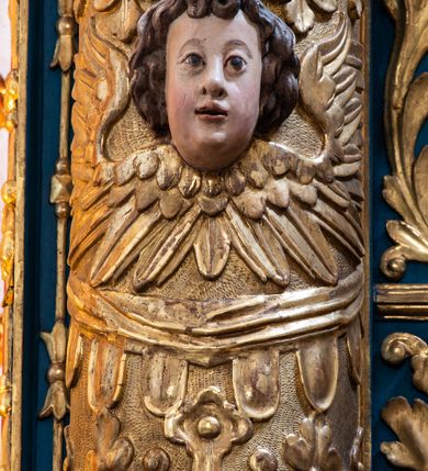 Zdjęcie nr 20: Ołtarz architektoniczny, trójosiowy, dwukondygnacyjny ze zwieńczeniem. Mensa prostopadłościenna, kamienna z drewnianym antepedium w formie leżącego prostokąta z postacią św. Augustyna ujętego wicią suchego akantu z przeplecioną, karbowaną wstążką i bukietami kwiatów. Przedstawienie otoczone profilowaną, ażurową ramą wypełnioną podobną wicią z akantu i kwiatów. Na mensie prostopadłościenne tabernakulum w formie kapliczki. Ściana frontowa z drzwiczkami w kształcie stojącego prostokąta dekorowanego krzyżem łacińskim ujętym wicią roślinną, zwieńczona trójkątnym przyczółkiem. Ścianka ujęta lizenami wypełnionymi wicią akantową podtrzymującymi pełne belkowanie obiegające bryłę, z mocno wysuniętym gzymsem wyłamanym w narożach. Całość zwieńczona czterospadowym dachem dekorowanym łuską. Na dachu baranek Boży leżący na księdze z siedmioma pieczęciami, przytrzymujący chorągiew, ukazany na tle chrystogramu otoczonego glorią promienistą. 
Nastawa na dwudzielnym cokole z półkolistymi bramkami ze zwieńczeniem utworzonym z ornamentu okuciowego ujmującego owalne pola. Osie pierwszej kondygnacji wydzielone kolumnami stojącymi na konsolach dekorowanych z frontu uskrzydlonymi główkami anielskimi powyżej liści akantu, na krawędziach cekinami, a po bokach wicią. Kolumny zostały przedzielone opaską w jednej trzeciej wysokości, dekorowane na całej wysokości wicią roślinną, główkami anielskimi w dolnej partii i imitacją kameryzacji na opaskach oraz w dwóch trzecich wysokości. Kolumny są ustawione na tle pilastrów dekorowanych wicią roślinną i zawieszonymi na niej chustkami. W polu centralnym kondygnacji jest nisza w kształcie stojącego prostokąta zamkniętego łukiem pełnym z postacią ukrzyżowanego Chrystusa na tle widoku Jerozolimy. W osiach bocznych mniejsze, ujęte pilastrami nisze o podobnym kształcie, których konchy wypełnione są muszlą, zwieńczone trójkątnym przyczółkiem przerwanym na cokół. W nich, na dekorowanych wicią i rozetami konsolach ustawiono figury: po lewej stronie św. Piotra, a po prawej św. Pawła. Kondygnacje ujmują ażurowe uszaki utworzone z ornamentu okuciowego, ulistnionych wolut i przewieszonej chustki. Kolumny podtrzymują pełne belkowanie wyniesione w łuk nad polem centralnym. Podłucze dekorowane rozetami, fryz głowami anielskimi i wicią, gzyms m.in. kostkowaniem i liśćmi akantu. Całość spięta kluczem z kartuszem z herbem kanoników regularnych od pokuty (marków). Na wyniesieniu belkowania posadowiono postaci aniołów trzymających narzędzia męki: anioł po lewej włócznię, a anioł po prawej gąbkę. Górna kondygnacja oparta została na schemacie aediculi – prostokątne pole ujęto kolumnami podtrzymującymi pełne belkowanie i trójkątny przyczółek przerwany na środku na cokół, na którym ustawiono rzeźbę  pelikana karmiącego młode własną krwią. Na krawędziach przyczółka dwie leżące postaci. Kondygnacja flankowana postaciami czterech ewangelistów ustawionymi na cokołach. Po lewej stronie św. Marek i św. Jan, po prawej św. Mateusz i św. Łukasz. Struktura polichromowana na kolor ciemnoniebieski; kolumny, profile, detale i ornamenty złocone i srebrzone.
