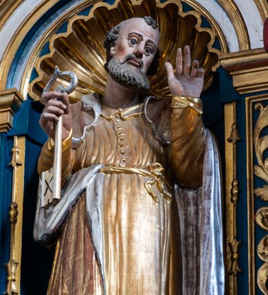 Zdjęcie nr 21: Ołtarz architektoniczny, trójosiowy, dwukondygnacyjny ze zwieńczeniem. Mensa prostopadłościenna, kamienna z drewnianym antepedium w formie leżącego prostokąta z postacią św. Augustyna ujętego wicią suchego akantu z przeplecioną, karbowaną wstążką i bukietami kwiatów. Przedstawienie otoczone profilowaną, ażurową ramą wypełnioną podobną wicią z akantu i kwiatów. Na mensie prostopadłościenne tabernakulum w formie kapliczki. Ściana frontowa z drzwiczkami w kształcie stojącego prostokąta dekorowanego krzyżem łacińskim ujętym wicią roślinną, zwieńczona trójkątnym przyczółkiem. Ścianka ujęta lizenami wypełnionymi wicią akantową podtrzymującymi pełne belkowanie obiegające bryłę, z mocno wysuniętym gzymsem wyłamanym w narożach. Całość zwieńczona czterospadowym dachem dekorowanym łuską. Na dachu baranek Boży leżący na księdze z siedmioma pieczęciami, przytrzymujący chorągiew, ukazany na tle chrystogramu otoczonego glorią promienistą. 
Nastawa na dwudzielnym cokole z półkolistymi bramkami ze zwieńczeniem utworzonym z ornamentu okuciowego ujmującego owalne pola. Osie pierwszej kondygnacji wydzielone kolumnami stojącymi na konsolach dekorowanych z frontu uskrzydlonymi główkami anielskimi powyżej liści akantu, na krawędziach cekinami, a po bokach wicią. Kolumny zostały przedzielone opaską w jednej trzeciej wysokości, dekorowane na całej wysokości wicią roślinną, główkami anielskimi w dolnej partii i imitacją kameryzacji na opaskach oraz w dwóch trzecich wysokości. Kolumny są ustawione na tle pilastrów dekorowanych wicią roślinną i zawieszonymi na niej chustkami. W polu centralnym kondygnacji jest nisza w kształcie stojącego prostokąta zamkniętego łukiem pełnym z postacią ukrzyżowanego Chrystusa na tle widoku Jerozolimy. W osiach bocznych mniejsze, ujęte pilastrami nisze o podobnym kształcie, których konchy wypełnione są muszlą, zwieńczone trójkątnym przyczółkiem przerwanym na cokół. W nich, na dekorowanych wicią i rozetami konsolach ustawiono figury: po lewej stronie św. Piotra, a po prawej św. Pawła. Kondygnacje ujmują ażurowe uszaki utworzone z ornamentu okuciowego, ulistnionych wolut i przewieszonej chustki. Kolumny podtrzymują pełne belkowanie wyniesione w łuk nad polem centralnym. Podłucze dekorowane rozetami, fryz głowami anielskimi i wicią, gzyms m.in. kostkowaniem i liśćmi akantu. Całość spięta kluczem z kartuszem z herbem kanoników regularnych od pokuty (marków). Na wyniesieniu belkowania posadowiono postaci aniołów trzymających narzędzia męki: anioł po lewej włócznię, a anioł po prawej gąbkę. Górna kondygnacja oparta została na schemacie aediculi – prostokątne pole ujęto kolumnami podtrzymującymi pełne belkowanie i trójkątny przyczółek przerwany na środku na cokół, na którym ustawiono rzeźbę  pelikana karmiącego młode własną krwią. Na krawędziach przyczółka dwie leżące postaci. Kondygnacja flankowana postaciami czterech ewangelistów ustawionymi na cokołach. Po lewej stronie św. Marek i św. Jan, po prawej św. Mateusz i św. Łukasz. Struktura polichromowana na kolor ciemnoniebieski; kolumny, profile, detale i ornamenty złocone i srebrzone.
