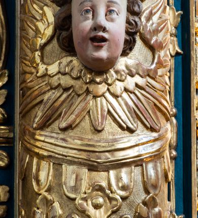 Zdjęcie nr 23: Ołtarz architektoniczny, trójosiowy, dwukondygnacyjny ze zwieńczeniem. Mensa prostopadłościenna, kamienna z drewnianym antepedium w formie leżącego prostokąta z postacią św. Augustyna ujętego wicią suchego akantu z przeplecioną, karbowaną wstążką i bukietami kwiatów. Przedstawienie otoczone profilowaną, ażurową ramą wypełnioną podobną wicią z akantu i kwiatów. Na mensie prostopadłościenne tabernakulum w formie kapliczki. Ściana frontowa z drzwiczkami w kształcie stojącego prostokąta dekorowanego krzyżem łacińskim ujętym wicią roślinną, zwieńczona trójkątnym przyczółkiem. Ścianka ujęta lizenami wypełnionymi wicią akantową podtrzymującymi pełne belkowanie obiegające bryłę, z mocno wysuniętym gzymsem wyłamanym w narożach. Całość zwieńczona czterospadowym dachem dekorowanym łuską. Na dachu baranek Boży leżący na księdze z siedmioma pieczęciami, przytrzymujący chorągiew, ukazany na tle chrystogramu otoczonego glorią promienistą. 
Nastawa na dwudzielnym cokole z półkolistymi bramkami ze zwieńczeniem utworzonym z ornamentu okuciowego ujmującego owalne pola. Osie pierwszej kondygnacji wydzielone kolumnami stojącymi na konsolach dekorowanych z frontu uskrzydlonymi główkami anielskimi powyżej liści akantu, na krawędziach cekinami, a po bokach wicią. Kolumny zostały przedzielone opaską w jednej trzeciej wysokości, dekorowane na całej wysokości wicią roślinną, główkami anielskimi w dolnej partii i imitacją kameryzacji na opaskach oraz w dwóch trzecich wysokości. Kolumny są ustawione na tle pilastrów dekorowanych wicią roślinną i zawieszonymi na niej chustkami. W polu centralnym kondygnacji jest nisza w kształcie stojącego prostokąta zamkniętego łukiem pełnym z postacią ukrzyżowanego Chrystusa na tle widoku Jerozolimy. W osiach bocznych mniejsze, ujęte pilastrami nisze o podobnym kształcie, których konchy wypełnione są muszlą, zwieńczone trójkątnym przyczółkiem przerwanym na cokół. W nich, na dekorowanych wicią i rozetami konsolach ustawiono figury: po lewej stronie św. Piotra, a po prawej św. Pawła. Kondygnacje ujmują ażurowe uszaki utworzone z ornamentu okuciowego, ulistnionych wolut i przewieszonej chustki. Kolumny podtrzymują pełne belkowanie wyniesione w łuk nad polem centralnym. Podłucze dekorowane rozetami, fryz głowami anielskimi i wicią, gzyms m.in. kostkowaniem i liśćmi akantu. Całość spięta kluczem z kartuszem z herbem kanoników regularnych od pokuty (marków). Na wyniesieniu belkowania posadowiono postaci aniołów trzymających narzędzia męki: anioł po lewej włócznię, a anioł po prawej gąbkę. Górna kondygnacja oparta została na schemacie aediculi – prostokątne pole ujęto kolumnami podtrzymującymi pełne belkowanie i trójkątny przyczółek przerwany na środku na cokół, na którym ustawiono rzeźbę  pelikana karmiącego młode własną krwią. Na krawędziach przyczółka dwie leżące postaci. Kondygnacja flankowana postaciami czterech ewangelistów ustawionymi na cokołach. Po lewej stronie św. Marek i św. Jan, po prawej św. Mateusz i św. Łukasz. Struktura polichromowana na kolor ciemnoniebieski; kolumny, profile, detale i ornamenty złocone i srebrzone.
