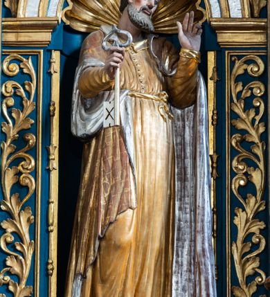 Zdjęcie nr 26: Ołtarz architektoniczny, trójosiowy, dwukondygnacyjny ze zwieńczeniem. Mensa prostopadłościenna, kamienna z drewnianym antepedium w formie leżącego prostokąta z postacią św. Augustyna ujętego wicią suchego akantu z przeplecioną, karbowaną wstążką i bukietami kwiatów. Przedstawienie otoczone profilowaną, ażurową ramą wypełnioną podobną wicią z akantu i kwiatów. Na mensie prostopadłościenne tabernakulum w formie kapliczki. Ściana frontowa z drzwiczkami w kształcie stojącego prostokąta dekorowanego krzyżem łacińskim ujętym wicią roślinną, zwieńczona trójkątnym przyczółkiem. Ścianka ujęta lizenami wypełnionymi wicią akantową podtrzymującymi pełne belkowanie obiegające bryłę, z mocno wysuniętym gzymsem wyłamanym w narożach. Całość zwieńczona czterospadowym dachem dekorowanym łuską. Na dachu baranek Boży leżący na księdze z siedmioma pieczęciami, przytrzymujący chorągiew, ukazany na tle chrystogramu otoczonego glorią promienistą. 
Nastawa na dwudzielnym cokole z półkolistymi bramkami ze zwieńczeniem utworzonym z ornamentu okuciowego ujmującego owalne pola. Osie pierwszej kondygnacji wydzielone kolumnami stojącymi na konsolach dekorowanych z frontu uskrzydlonymi główkami anielskimi powyżej liści akantu, na krawędziach cekinami, a po bokach wicią. Kolumny zostały przedzielone opaską w jednej trzeciej wysokości, dekorowane na całej wysokości wicią roślinną, główkami anielskimi w dolnej partii i imitacją kameryzacji na opaskach oraz w dwóch trzecich wysokości. Kolumny są ustawione na tle pilastrów dekorowanych wicią roślinną i zawieszonymi na niej chustkami. W polu centralnym kondygnacji jest nisza w kształcie stojącego prostokąta zamkniętego łukiem pełnym z postacią ukrzyżowanego Chrystusa na tle widoku Jerozolimy. W osiach bocznych mniejsze, ujęte pilastrami nisze o podobnym kształcie, których konchy wypełnione są muszlą, zwieńczone trójkątnym przyczółkiem przerwanym na cokół. W nich, na dekorowanych wicią i rozetami konsolach ustawiono figury: po lewej stronie św. Piotra, a po prawej św. Pawła. Kondygnacje ujmują ażurowe uszaki utworzone z ornamentu okuciowego, ulistnionych wolut i przewieszonej chustki. Kolumny podtrzymują pełne belkowanie wyniesione w łuk nad polem centralnym. Podłucze dekorowane rozetami, fryz głowami anielskimi i wicią, gzyms m.in. kostkowaniem i liśćmi akantu. Całość spięta kluczem z kartuszem z herbem kanoników regularnych od pokuty (marków). Na wyniesieniu belkowania posadowiono postaci aniołów trzymających narzędzia męki: anioł po lewej włócznię, a anioł po prawej gąbkę. Górna kondygnacja oparta została na schemacie aediculi – prostokątne pole ujęto kolumnami podtrzymującymi pełne belkowanie i trójkątny przyczółek przerwany na środku na cokół, na którym ustawiono rzeźbę  pelikana karmiącego młode własną krwią. Na krawędziach przyczółka dwie leżące postaci. Kondygnacja flankowana postaciami czterech ewangelistów ustawionymi na cokołach. Po lewej stronie św. Marek i św. Jan, po prawej św. Mateusz i św. Łukasz. Struktura polichromowana na kolor ciemnoniebieski; kolumny, profile, detale i ornamenty złocone i srebrzone.
