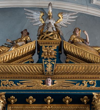 Zdjęcie nr 33: Ołtarz architektoniczny, trójosiowy, dwukondygnacyjny ze zwieńczeniem. Mensa prostopadłościenna, kamienna z drewnianym antepedium w formie leżącego prostokąta z postacią św. Augustyna ujętego wicią suchego akantu z przeplecioną, karbowaną wstążką i bukietami kwiatów. Przedstawienie otoczone profilowaną, ażurową ramą wypełnioną podobną wicią z akantu i kwiatów. Na mensie prostopadłościenne tabernakulum w formie kapliczki. Ściana frontowa z drzwiczkami w kształcie stojącego prostokąta dekorowanego krzyżem łacińskim ujętym wicią roślinną, zwieńczona trójkątnym przyczółkiem. Ścianka ujęta lizenami wypełnionymi wicią akantową podtrzymującymi pełne belkowanie obiegające bryłę, z mocno wysuniętym gzymsem wyłamanym w narożach. Całość zwieńczona czterospadowym dachem dekorowanym łuską. Na dachu baranek Boży leżący na księdze z siedmioma pieczęciami, przytrzymujący chorągiew, ukazany na tle chrystogramu otoczonego glorią promienistą. 
Nastawa na dwudzielnym cokole z półkolistymi bramkami ze zwieńczeniem utworzonym z ornamentu okuciowego ujmującego owalne pola. Osie pierwszej kondygnacji wydzielone kolumnami stojącymi na konsolach dekorowanych z frontu uskrzydlonymi główkami anielskimi powyżej liści akantu, na krawędziach cekinami, a po bokach wicią. Kolumny zostały przedzielone opaską w jednej trzeciej wysokości, dekorowane na całej wysokości wicią roślinną, główkami anielskimi w dolnej partii i imitacją kameryzacji na opaskach oraz w dwóch trzecich wysokości. Kolumny są ustawione na tle pilastrów dekorowanych wicią roślinną i zawieszonymi na niej chustkami. W polu centralnym kondygnacji jest nisza w kształcie stojącego prostokąta zamkniętego łukiem pełnym z postacią ukrzyżowanego Chrystusa na tle widoku Jerozolimy. W osiach bocznych mniejsze, ujęte pilastrami nisze o podobnym kształcie, których konchy wypełnione są muszlą, zwieńczone trójkątnym przyczółkiem przerwanym na cokół. W nich, na dekorowanych wicią i rozetami konsolach ustawiono figury: po lewej stronie św. Piotra, a po prawej św. Pawła. Kondygnacje ujmują ażurowe uszaki utworzone z ornamentu okuciowego, ulistnionych wolut i przewieszonej chustki. Kolumny podtrzymują pełne belkowanie wyniesione w łuk nad polem centralnym. Podłucze dekorowane rozetami, fryz głowami anielskimi i wicią, gzyms m.in. kostkowaniem i liśćmi akantu. Całość spięta kluczem z kartuszem z herbem kanoników regularnych od pokuty (marków). Na wyniesieniu belkowania posadowiono postaci aniołów trzymających narzędzia męki: anioł po lewej włócznię, a anioł po prawej gąbkę. Górna kondygnacja oparta została na schemacie aediculi – prostokątne pole ujęto kolumnami podtrzymującymi pełne belkowanie i trójkątny przyczółek przerwany na środku na cokół, na którym ustawiono rzeźbę  pelikana karmiącego młode własną krwią. Na krawędziach przyczółka dwie leżące postaci. Kondygnacja flankowana postaciami czterech ewangelistów ustawionymi na cokołach. Po lewej stronie św. Marek i św. Jan, po prawej św. Mateusz i św. Łukasz. Struktura polichromowana na kolor ciemnoniebieski; kolumny, profile, detale i ornamenty złocone i srebrzone.
