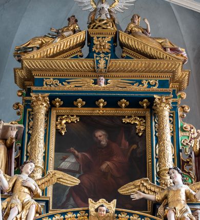 Zdjęcie nr 41: Ołtarz architektoniczny, trójosiowy, dwukondygnacyjny ze zwieńczeniem. Mensa prostopadłościenna, kamienna z drewnianym antepedium w formie leżącego prostokąta z postacią św. Augustyna ujętego wicią suchego akantu z przeplecioną, karbowaną wstążką i bukietami kwiatów. Przedstawienie otoczone profilowaną, ażurową ramą wypełnioną podobną wicią z akantu i kwiatów. Na mensie prostopadłościenne tabernakulum w formie kapliczki. Ściana frontowa z drzwiczkami w kształcie stojącego prostokąta dekorowanego krzyżem łacińskim ujętym wicią roślinną, zwieńczona trójkątnym przyczółkiem. Ścianka ujęta lizenami wypełnionymi wicią akantową podtrzymującymi pełne belkowanie obiegające bryłę, z mocno wysuniętym gzymsem wyłamanym w narożach. Całość zwieńczona czterospadowym dachem dekorowanym łuską. Na dachu baranek Boży leżący na księdze z siedmioma pieczęciami, przytrzymujący chorągiew, ukazany na tle chrystogramu otoczonego glorią promienistą. 
Nastawa na dwudzielnym cokole z półkolistymi bramkami ze zwieńczeniem utworzonym z ornamentu okuciowego ujmującego owalne pola. Osie pierwszej kondygnacji wydzielone kolumnami stojącymi na konsolach dekorowanych z frontu uskrzydlonymi główkami anielskimi powyżej liści akantu, na krawędziach cekinami, a po bokach wicią. Kolumny zostały przedzielone opaską w jednej trzeciej wysokości, dekorowane na całej wysokości wicią roślinną, główkami anielskimi w dolnej partii i imitacją kameryzacji na opaskach oraz w dwóch trzecich wysokości. Kolumny są ustawione na tle pilastrów dekorowanych wicią roślinną i zawieszonymi na niej chustkami. W polu centralnym kondygnacji jest nisza w kształcie stojącego prostokąta zamkniętego łukiem pełnym z postacią ukrzyżowanego Chrystusa na tle widoku Jerozolimy. W osiach bocznych mniejsze, ujęte pilastrami nisze o podobnym kształcie, których konchy wypełnione są muszlą, zwieńczone trójkątnym przyczółkiem przerwanym na cokół. W nich, na dekorowanych wicią i rozetami konsolach ustawiono figury: po lewej stronie św. Piotra, a po prawej św. Pawła. Kondygnacje ujmują ażurowe uszaki utworzone z ornamentu okuciowego, ulistnionych wolut i przewieszonej chustki. Kolumny podtrzymują pełne belkowanie wyniesione w łuk nad polem centralnym. Podłucze dekorowane rozetami, fryz głowami anielskimi i wicią, gzyms m.in. kostkowaniem i liśćmi akantu. Całość spięta kluczem z kartuszem z herbem kanoników regularnych od pokuty (marków). Na wyniesieniu belkowania posadowiono postaci aniołów trzymających narzędzia męki: anioł po lewej włócznię, a anioł po prawej gąbkę. Górna kondygnacja oparta została na schemacie aediculi – prostokątne pole ujęto kolumnami podtrzymującymi pełne belkowanie i trójkątny przyczółek przerwany na środku na cokół, na którym ustawiono rzeźbę  pelikana karmiącego młode własną krwią. Na krawędziach przyczółka dwie leżące postaci. Kondygnacja flankowana postaciami czterech ewangelistów ustawionymi na cokołach. Po lewej stronie św. Marek i św. Jan, po prawej św. Mateusz i św. Łukasz. Struktura polichromowana na kolor ciemnoniebieski; kolumny, profile, detale i ornamenty złocone i srebrzone.
