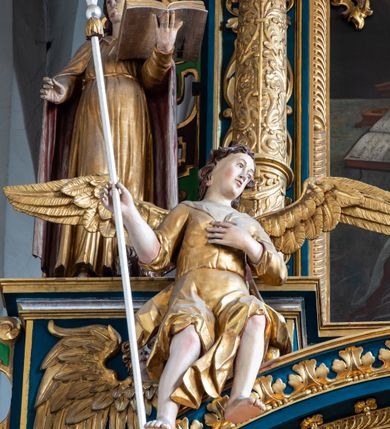 Zdjęcie nr 35: Ołtarz architektoniczny, trójosiowy, dwukondygnacyjny ze zwieńczeniem. Mensa prostopadłościenna, kamienna z drewnianym antepedium w formie leżącego prostokąta z postacią św. Augustyna ujętego wicią suchego akantu z przeplecioną, karbowaną wstążką i bukietami kwiatów. Przedstawienie otoczone profilowaną, ażurową ramą wypełnioną podobną wicią z akantu i kwiatów. Na mensie prostopadłościenne tabernakulum w formie kapliczki. Ściana frontowa z drzwiczkami w kształcie stojącego prostokąta dekorowanego krzyżem łacińskim ujętym wicią roślinną, zwieńczona trójkątnym przyczółkiem. Ścianka ujęta lizenami wypełnionymi wicią akantową podtrzymującymi pełne belkowanie obiegające bryłę, z mocno wysuniętym gzymsem wyłamanym w narożach. Całość zwieńczona czterospadowym dachem dekorowanym łuską. Na dachu baranek Boży leżący na księdze z siedmioma pieczęciami, przytrzymujący chorągiew, ukazany na tle chrystogramu otoczonego glorią promienistą. 
Nastawa na dwudzielnym cokole z półkolistymi bramkami ze zwieńczeniem utworzonym z ornamentu okuciowego ujmującego owalne pola. Osie pierwszej kondygnacji wydzielone kolumnami stojącymi na konsolach dekorowanych z frontu uskrzydlonymi główkami anielskimi powyżej liści akantu, na krawędziach cekinami, a po bokach wicią. Kolumny zostały przedzielone opaską w jednej trzeciej wysokości, dekorowane na całej wysokości wicią roślinną, główkami anielskimi w dolnej partii i imitacją kameryzacji na opaskach oraz w dwóch trzecich wysokości. Kolumny są ustawione na tle pilastrów dekorowanych wicią roślinną i zawieszonymi na niej chustkami. W polu centralnym kondygnacji jest nisza w kształcie stojącego prostokąta zamkniętego łukiem pełnym z postacią ukrzyżowanego Chrystusa na tle widoku Jerozolimy. W osiach bocznych mniejsze, ujęte pilastrami nisze o podobnym kształcie, których konchy wypełnione są muszlą, zwieńczone trójkątnym przyczółkiem przerwanym na cokół. W nich, na dekorowanych wicią i rozetami konsolach ustawiono figury: po lewej stronie św. Piotra, a po prawej św. Pawła. Kondygnacje ujmują ażurowe uszaki utworzone z ornamentu okuciowego, ulistnionych wolut i przewieszonej chustki. Kolumny podtrzymują pełne belkowanie wyniesione w łuk nad polem centralnym. Podłucze dekorowane rozetami, fryz głowami anielskimi i wicią, gzyms m.in. kostkowaniem i liśćmi akantu. Całość spięta kluczem z kartuszem z herbem kanoników regularnych od pokuty (marków). Na wyniesieniu belkowania posadowiono postaci aniołów trzymających narzędzia męki: anioł po lewej włócznię, a anioł po prawej gąbkę. Górna kondygnacja oparta została na schemacie aediculi – prostokątne pole ujęto kolumnami podtrzymującymi pełne belkowanie i trójkątny przyczółek przerwany na środku na cokół, na którym ustawiono rzeźbę  pelikana karmiącego młode własną krwią. Na krawędziach przyczółka dwie leżące postaci. Kondygnacja flankowana postaciami czterech ewangelistów ustawionymi na cokołach. Po lewej stronie św. Marek i św. Jan, po prawej św. Mateusz i św. Łukasz. Struktura polichromowana na kolor ciemnoniebieski; kolumny, profile, detale i ornamenty złocone i srebrzone.
