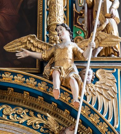Zdjęcie nr 34: Ołtarz architektoniczny, trójosiowy, dwukondygnacyjny ze zwieńczeniem. Mensa prostopadłościenna, kamienna z drewnianym antepedium w formie leżącego prostokąta z postacią św. Augustyna ujętego wicią suchego akantu z przeplecioną, karbowaną wstążką i bukietami kwiatów. Przedstawienie otoczone profilowaną, ażurową ramą wypełnioną podobną wicią z akantu i kwiatów. Na mensie prostopadłościenne tabernakulum w formie kapliczki. Ściana frontowa z drzwiczkami w kształcie stojącego prostokąta dekorowanego krzyżem łacińskim ujętym wicią roślinną, zwieńczona trójkątnym przyczółkiem. Ścianka ujęta lizenami wypełnionymi wicią akantową podtrzymującymi pełne belkowanie obiegające bryłę, z mocno wysuniętym gzymsem wyłamanym w narożach. Całość zwieńczona czterospadowym dachem dekorowanym łuską. Na dachu baranek Boży leżący na księdze z siedmioma pieczęciami, przytrzymujący chorągiew, ukazany na tle chrystogramu otoczonego glorią promienistą. 
Nastawa na dwudzielnym cokole z półkolistymi bramkami ze zwieńczeniem utworzonym z ornamentu okuciowego ujmującego owalne pola. Osie pierwszej kondygnacji wydzielone kolumnami stojącymi na konsolach dekorowanych z frontu uskrzydlonymi główkami anielskimi powyżej liści akantu, na krawędziach cekinami, a po bokach wicią. Kolumny zostały przedzielone opaską w jednej trzeciej wysokości, dekorowane na całej wysokości wicią roślinną, główkami anielskimi w dolnej partii i imitacją kameryzacji na opaskach oraz w dwóch trzecich wysokości. Kolumny są ustawione na tle pilastrów dekorowanych wicią roślinną i zawieszonymi na niej chustkami. W polu centralnym kondygnacji jest nisza w kształcie stojącego prostokąta zamkniętego łukiem pełnym z postacią ukrzyżowanego Chrystusa na tle widoku Jerozolimy. W osiach bocznych mniejsze, ujęte pilastrami nisze o podobnym kształcie, których konchy wypełnione są muszlą, zwieńczone trójkątnym przyczółkiem przerwanym na cokół. W nich, na dekorowanych wicią i rozetami konsolach ustawiono figury: po lewej stronie św. Piotra, a po prawej św. Pawła. Kondygnacje ujmują ażurowe uszaki utworzone z ornamentu okuciowego, ulistnionych wolut i przewieszonej chustki. Kolumny podtrzymują pełne belkowanie wyniesione w łuk nad polem centralnym. Podłucze dekorowane rozetami, fryz głowami anielskimi i wicią, gzyms m.in. kostkowaniem i liśćmi akantu. Całość spięta kluczem z kartuszem z herbem kanoników regularnych od pokuty (marków). Na wyniesieniu belkowania posadowiono postaci aniołów trzymających narzędzia męki: anioł po lewej włócznię, a anioł po prawej gąbkę. Górna kondygnacja oparta została na schemacie aediculi – prostokątne pole ujęto kolumnami podtrzymującymi pełne belkowanie i trójkątny przyczółek przerwany na środku na cokół, na którym ustawiono rzeźbę  pelikana karmiącego młode własną krwią. Na krawędziach przyczółka dwie leżące postaci. Kondygnacja flankowana postaciami czterech ewangelistów ustawionymi na cokołach. Po lewej stronie św. Marek i św. Jan, po prawej św. Mateusz i św. Łukasz. Struktura polichromowana na kolor ciemnoniebieski; kolumny, profile, detale i ornamenty złocone i srebrzone.
