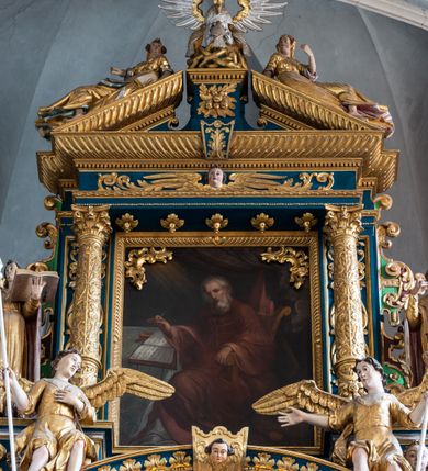 Zdjęcie nr 42: Ołtarz architektoniczny, trójosiowy, dwukondygnacyjny ze zwieńczeniem. Mensa prostopadłościenna, kamienna z drewnianym antepedium w formie leżącego prostokąta z postacią św. Augustyna ujętego wicią suchego akantu z przeplecioną, karbowaną wstążką i bukietami kwiatów. Przedstawienie otoczone profilowaną, ażurową ramą wypełnioną podobną wicią z akantu i kwiatów. Na mensie prostopadłościenne tabernakulum w formie kapliczki. Ściana frontowa z drzwiczkami w kształcie stojącego prostokąta dekorowanego krzyżem łacińskim ujętym wicią roślinną, zwieńczona trójkątnym przyczółkiem. Ścianka ujęta lizenami wypełnionymi wicią akantową podtrzymującymi pełne belkowanie obiegające bryłę, z mocno wysuniętym gzymsem wyłamanym w narożach. Całość zwieńczona czterospadowym dachem dekorowanym łuską. Na dachu baranek Boży leżący na księdze z siedmioma pieczęciami, przytrzymujący chorągiew, ukazany na tle chrystogramu otoczonego glorią promienistą. 
Nastawa na dwudzielnym cokole z półkolistymi bramkami ze zwieńczeniem utworzonym z ornamentu okuciowego ujmującego owalne pola. Osie pierwszej kondygnacji wydzielone kolumnami stojącymi na konsolach dekorowanych z frontu uskrzydlonymi główkami anielskimi powyżej liści akantu, na krawędziach cekinami, a po bokach wicią. Kolumny zostały przedzielone opaską w jednej trzeciej wysokości, dekorowane na całej wysokości wicią roślinną, główkami anielskimi w dolnej partii i imitacją kameryzacji na opaskach oraz w dwóch trzecich wysokości. Kolumny są ustawione na tle pilastrów dekorowanych wicią roślinną i zawieszonymi na niej chustkami. W polu centralnym kondygnacji jest nisza w kształcie stojącego prostokąta zamkniętego łukiem pełnym z postacią ukrzyżowanego Chrystusa na tle widoku Jerozolimy. W osiach bocznych mniejsze, ujęte pilastrami nisze o podobnym kształcie, których konchy wypełnione są muszlą, zwieńczone trójkątnym przyczółkiem przerwanym na cokół. W nich, na dekorowanych wicią i rozetami konsolach ustawiono figury: po lewej stronie św. Piotra, a po prawej św. Pawła. Kondygnacje ujmują ażurowe uszaki utworzone z ornamentu okuciowego, ulistnionych wolut i przewieszonej chustki. Kolumny podtrzymują pełne belkowanie wyniesione w łuk nad polem centralnym. Podłucze dekorowane rozetami, fryz głowami anielskimi i wicią, gzyms m.in. kostkowaniem i liśćmi akantu. Całość spięta kluczem z kartuszem z herbem kanoników regularnych od pokuty (marków). Na wyniesieniu belkowania posadowiono postaci aniołów trzymających narzędzia męki: anioł po lewej włócznię, a anioł po prawej gąbkę. Górna kondygnacja oparta została na schemacie aediculi – prostokątne pole ujęto kolumnami podtrzymującymi pełne belkowanie i trójkątny przyczółek przerwany na środku na cokół, na którym ustawiono rzeźbę  pelikana karmiącego młode własną krwią. Na krawędziach przyczółka dwie leżące postaci. Kondygnacja flankowana postaciami czterech ewangelistów ustawionymi na cokołach. Po lewej stronie św. Marek i św. Jan, po prawej św. Mateusz i św. Łukasz. Struktura polichromowana na kolor ciemnoniebieski; kolumny, profile, detale i ornamenty złocone i srebrzone.
